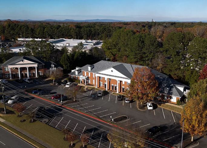 A parking lot with several buildings, trees with autumn leaves, and power lines in the foreground.