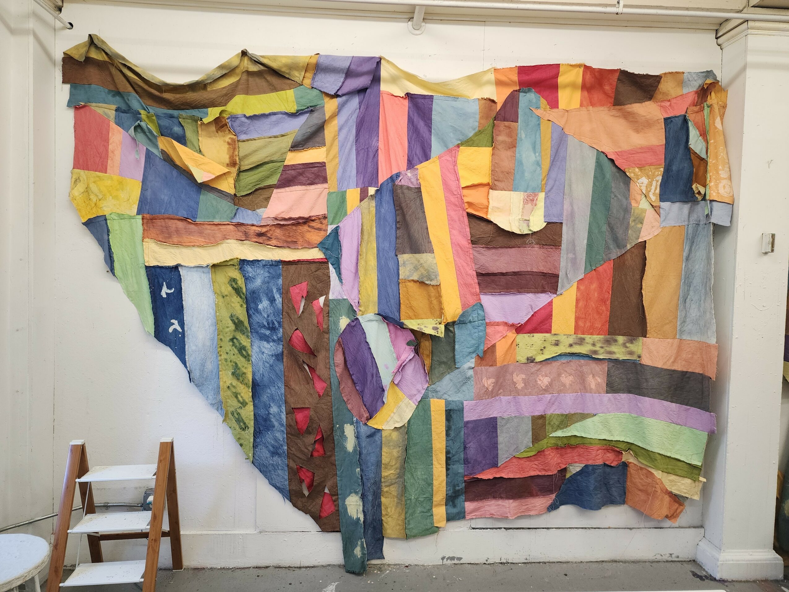 Colorful patchwork quilt hanging on a wall, with various fabric pieces in different shapes and colors.