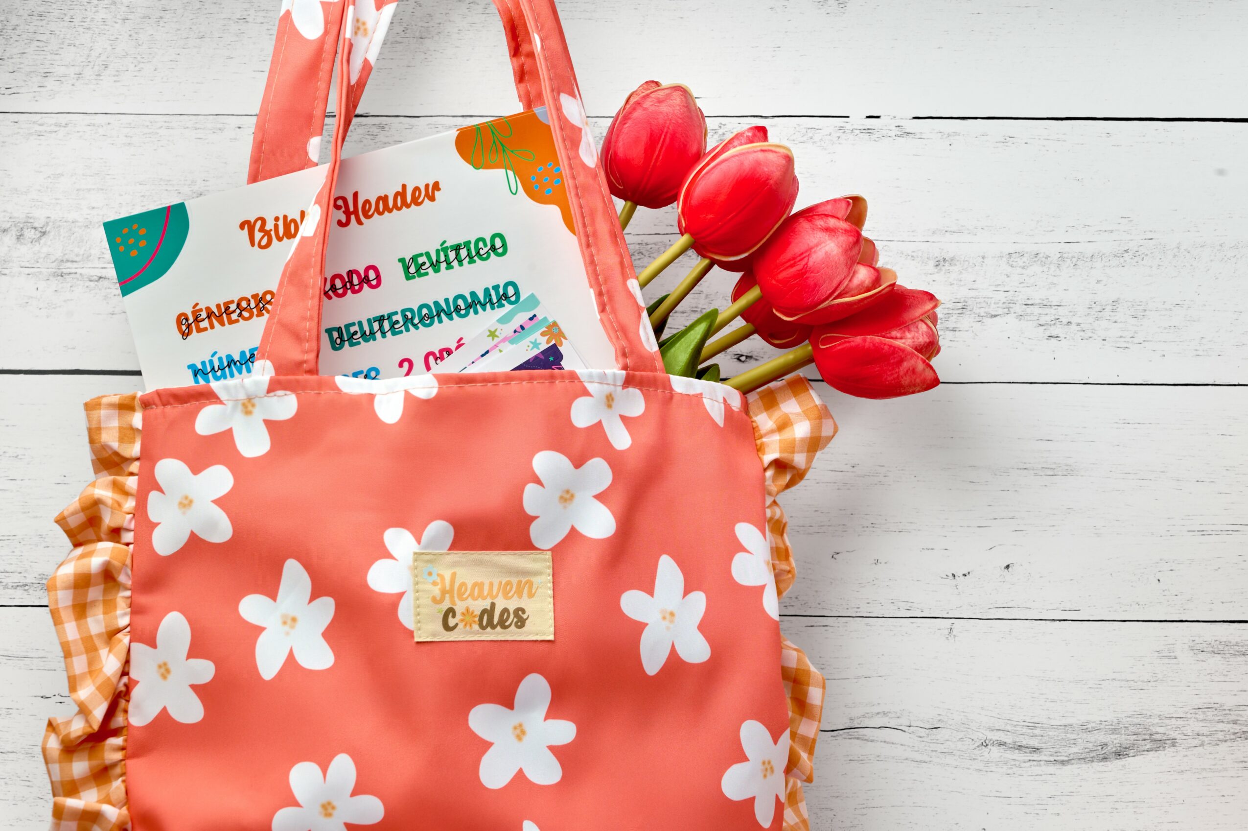 Pink bag with white flowers, red tulips, and colorful papers inside, on a white wooden surface.