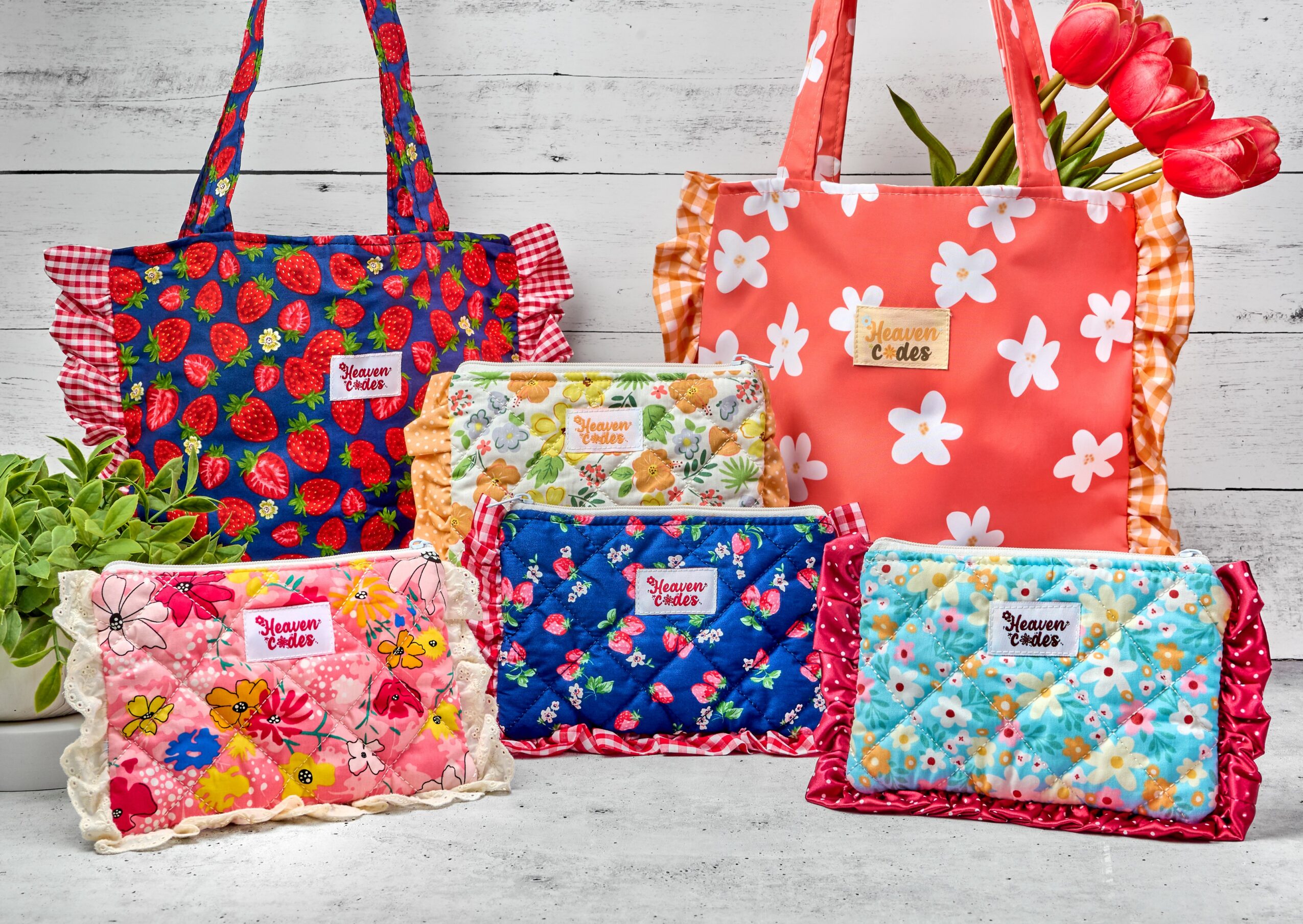 Six colorful fabric bags with floral and fruit patterns arranged on a white wooden surface, some with flowers nearby.