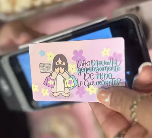 Person holding a card with a cartoon girl and colorful flowers, with handwritten message in Spanish.