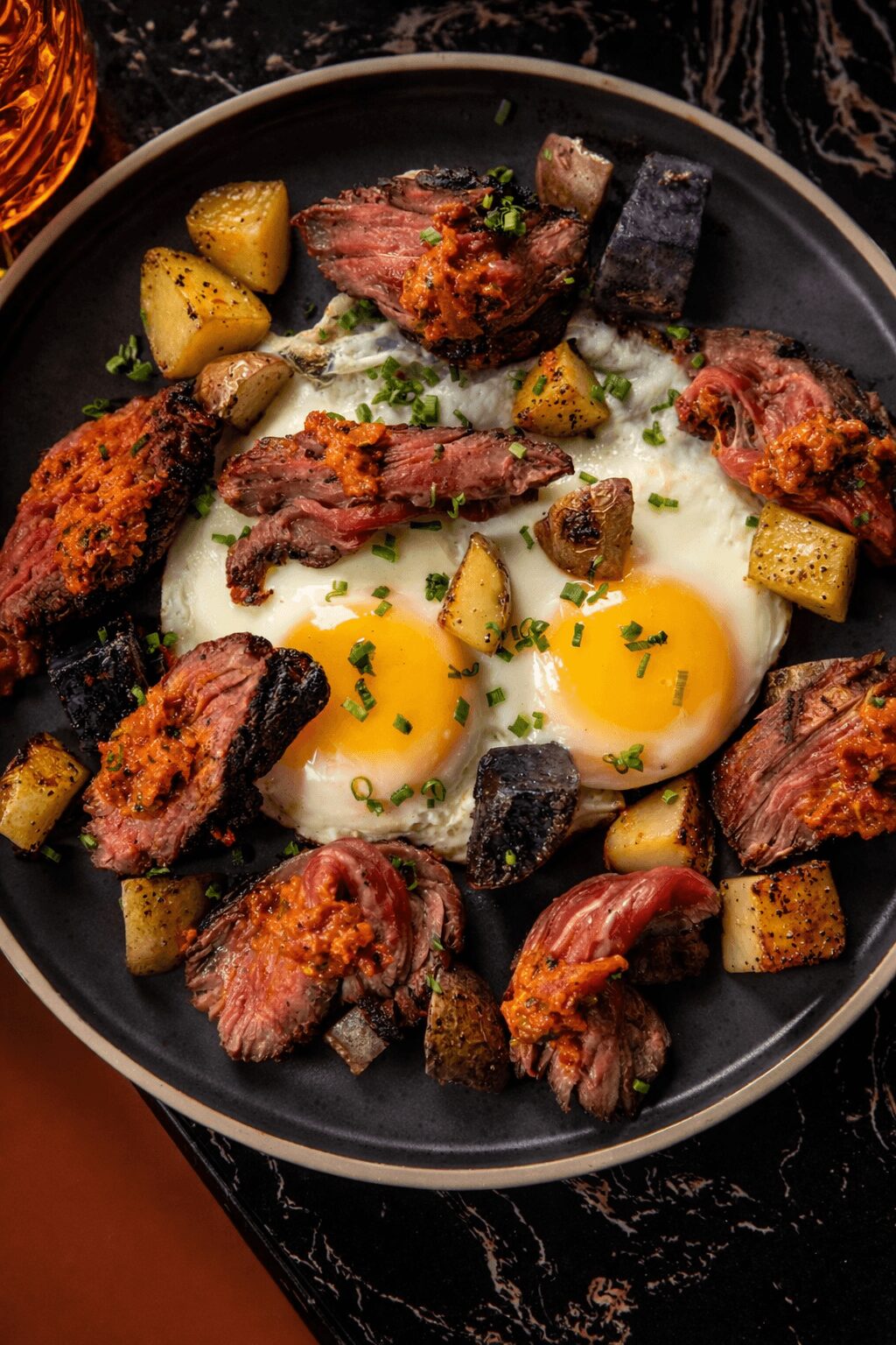 Fried eggs with runny yolks surrounded by cooked meat and roasted potatoes in a black skillet.