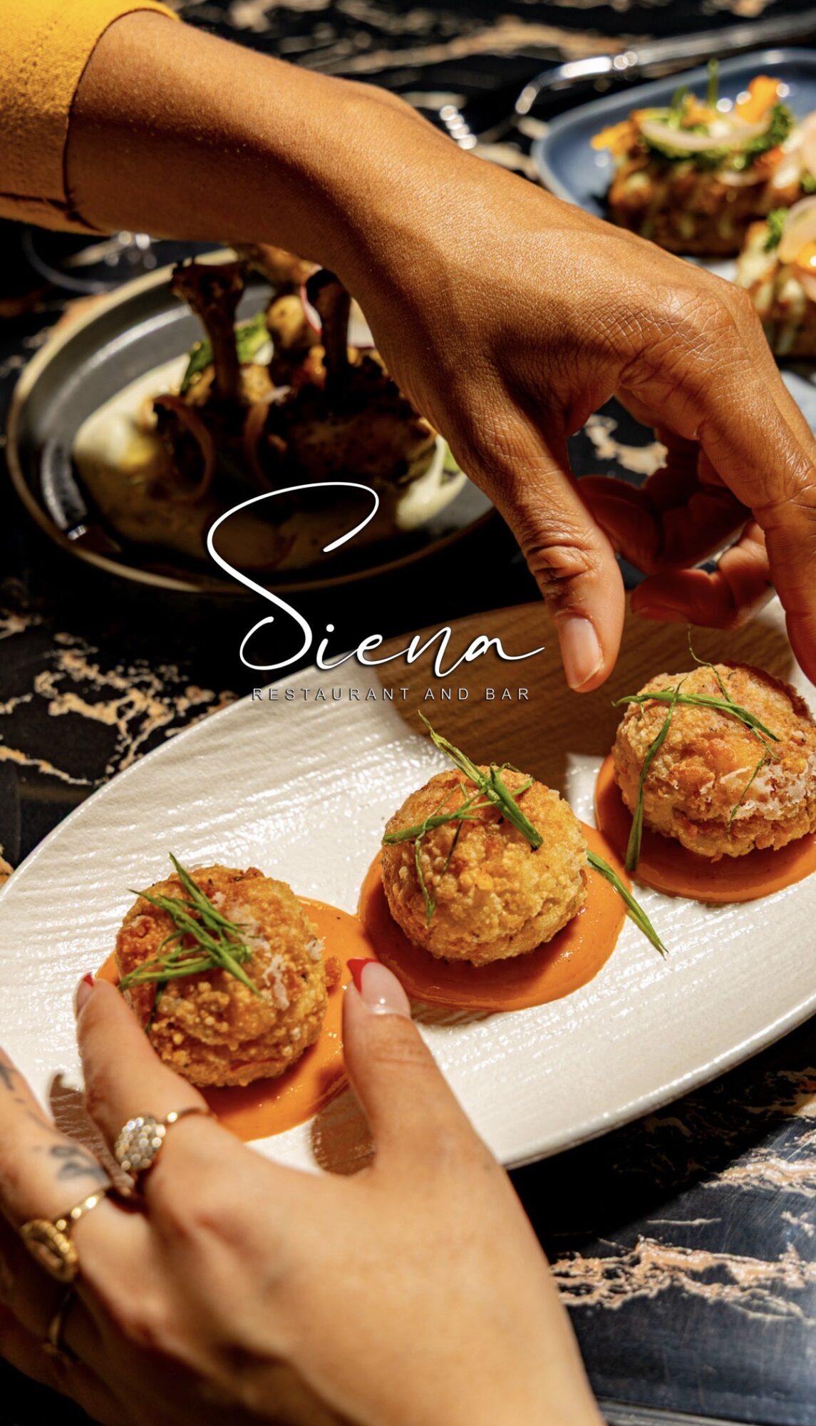 Person's hand reaching for a plate of three appetizers on a white dish, with other dishes in the background.