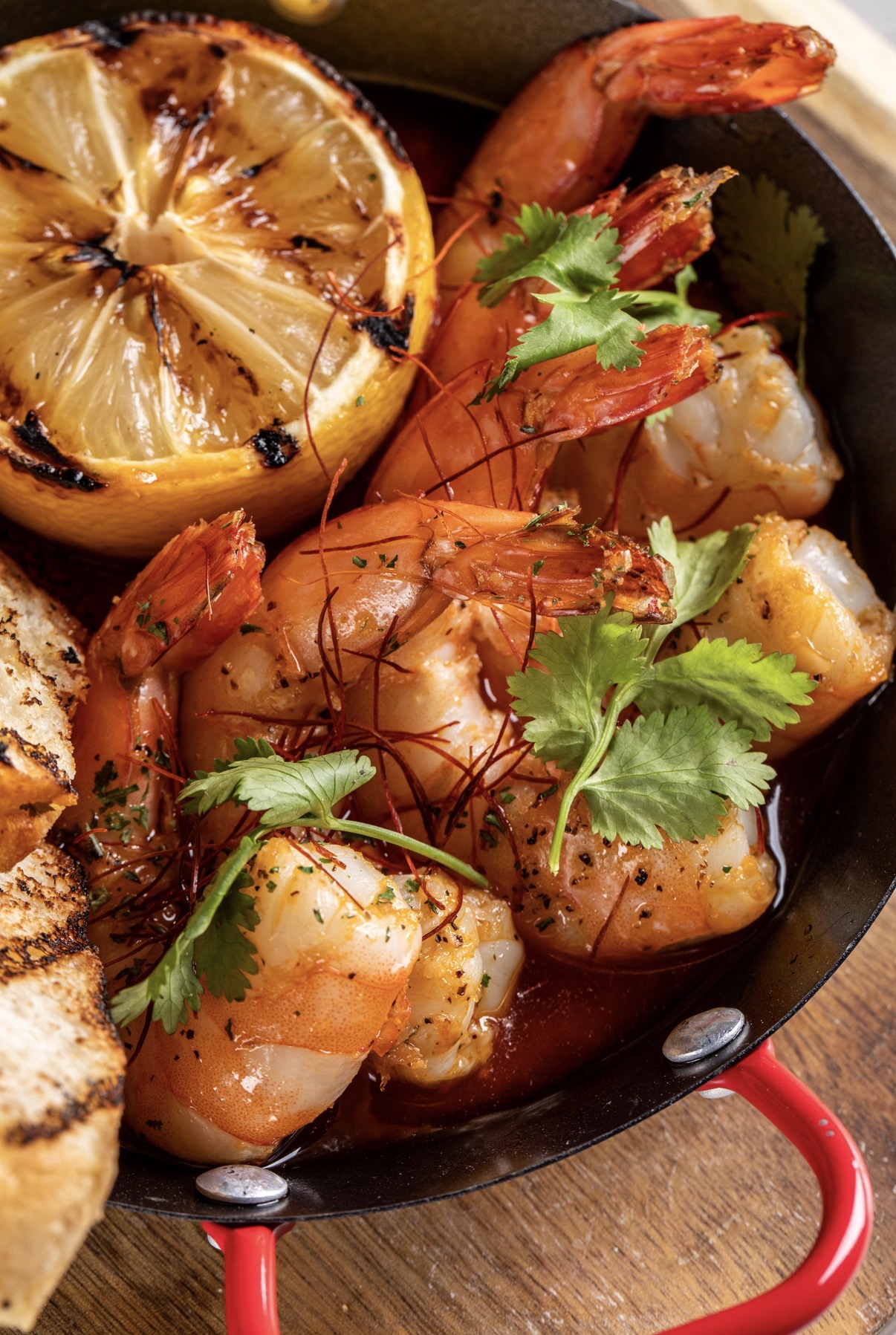 Shrimp with cilantro, grilled lemon half, and a piece of bread on a black plate.
