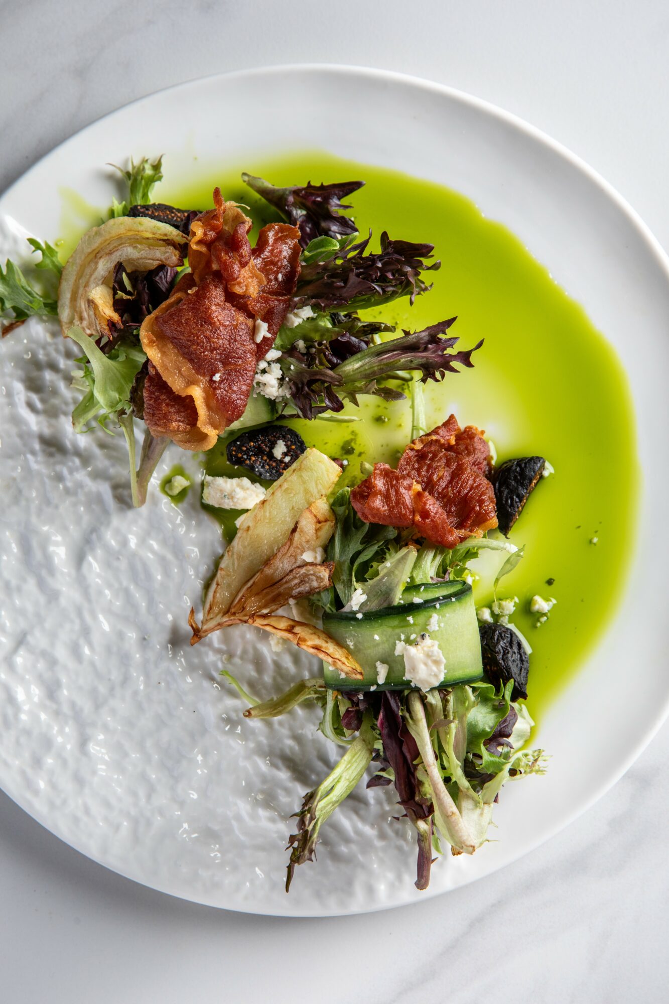 Plate with greens, crispy toppings, green sauce, and a white textured element on the side.