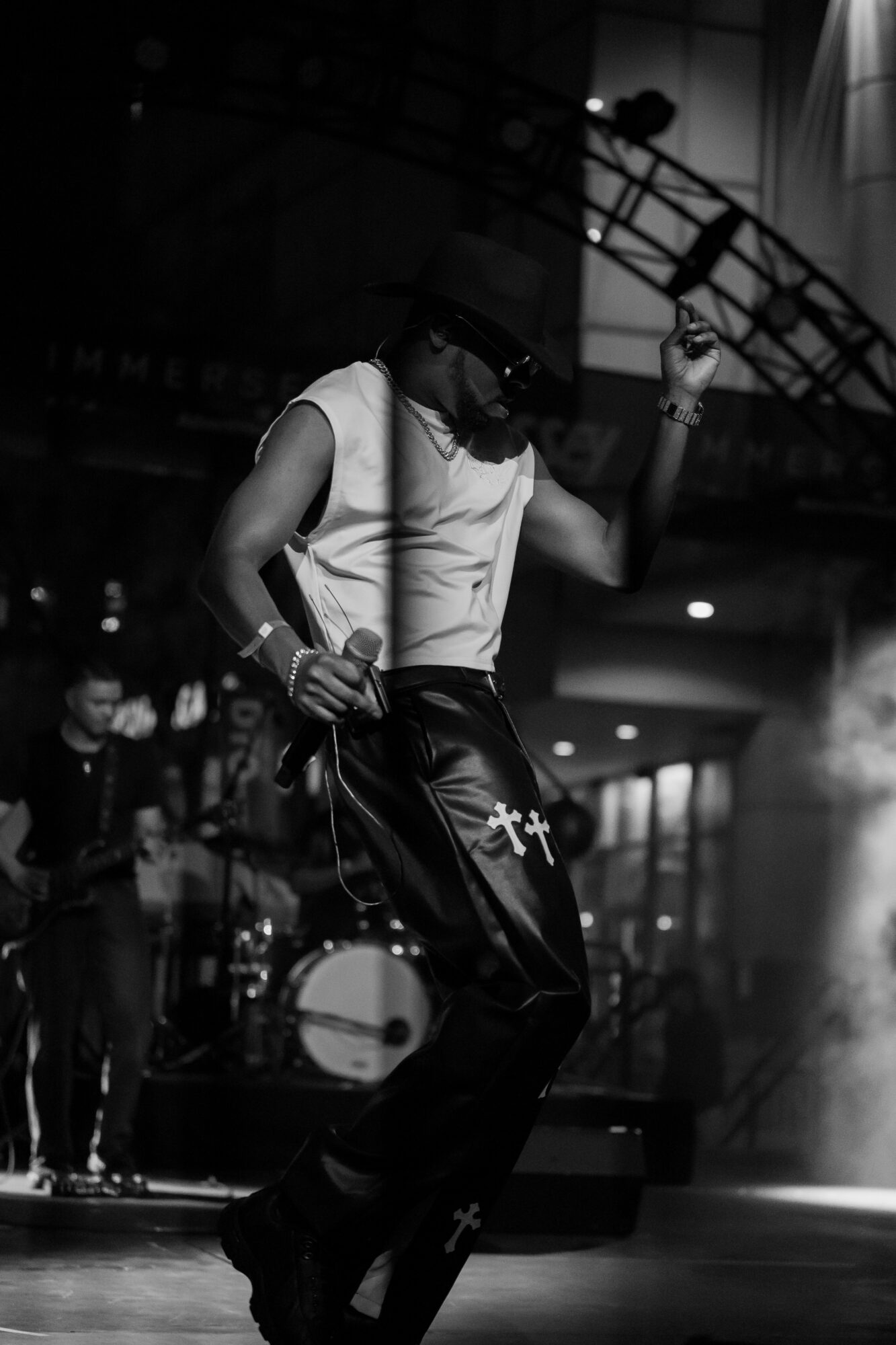Performer singing into microphone on stage with band, stage lights, and equipment visible in background.