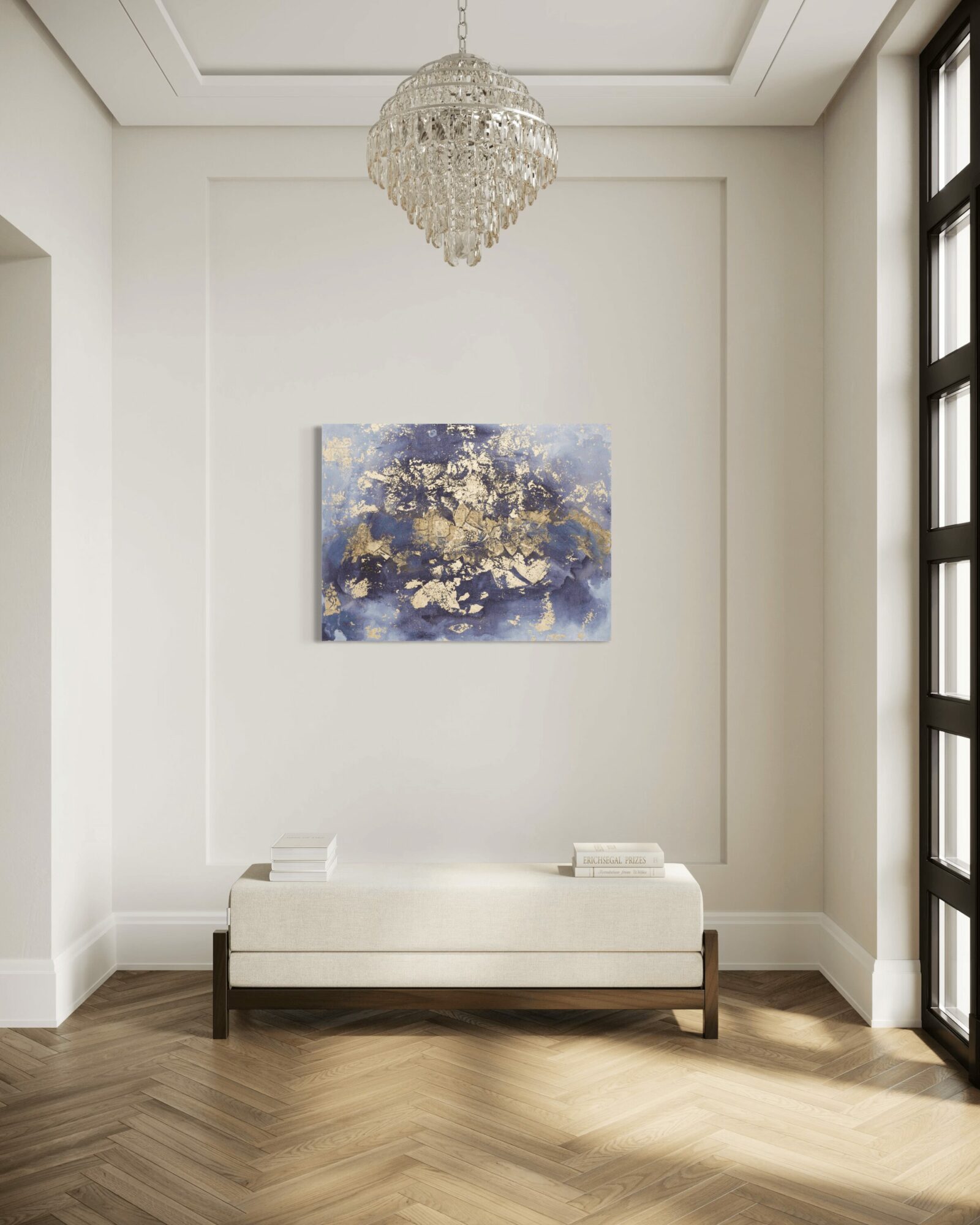 White bench with books on top, centered below a colorful abstract painting on a white wall, chandelier hanging from ceiling, sunlight streaming in.