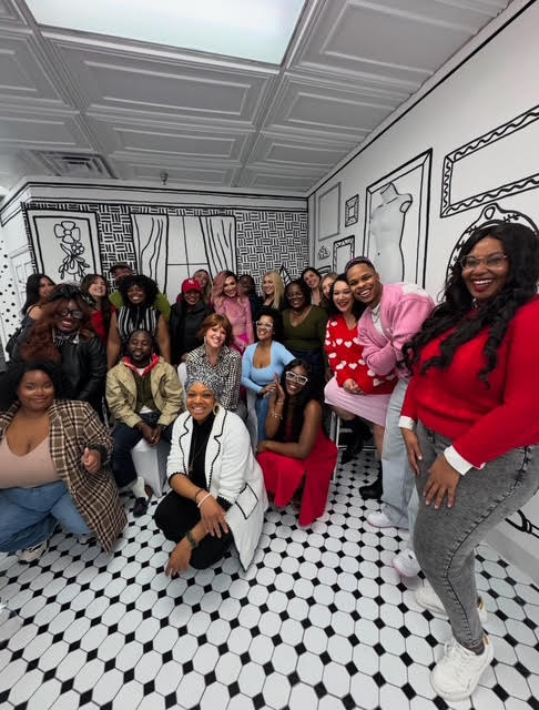 Group of diverse women smiling in a room with black and white patterned floor and wall art.