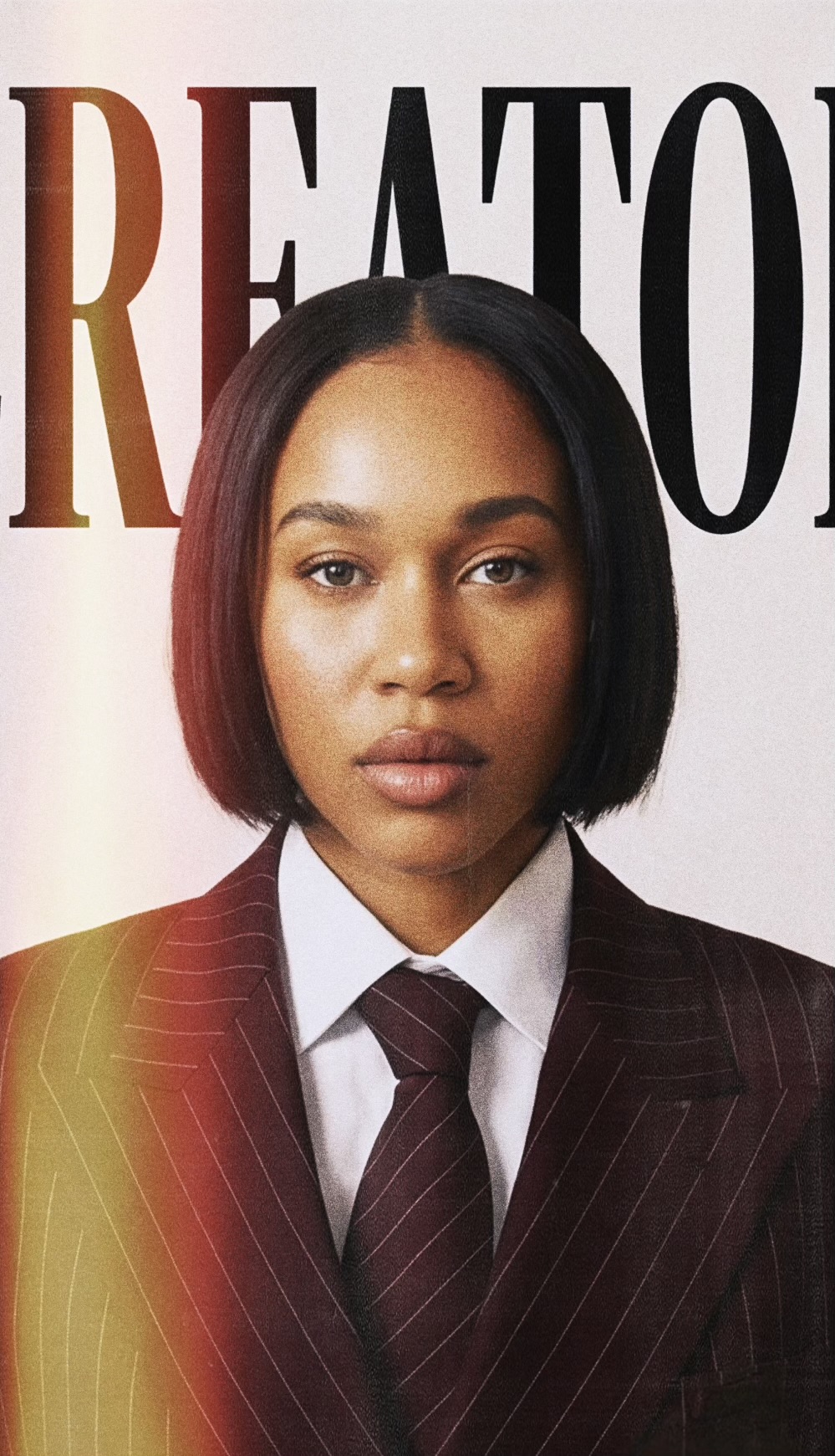 Portrait of a woman with shoulder-length black hair, wearing a dark pinstripe suit and tie, against a white background.
