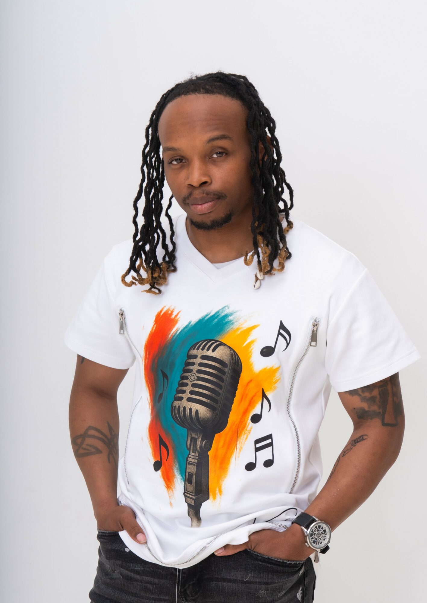 Man with long dreadlocks wearing a white T-shirt with a colorful microphone and musical notes, standing against a plain background.