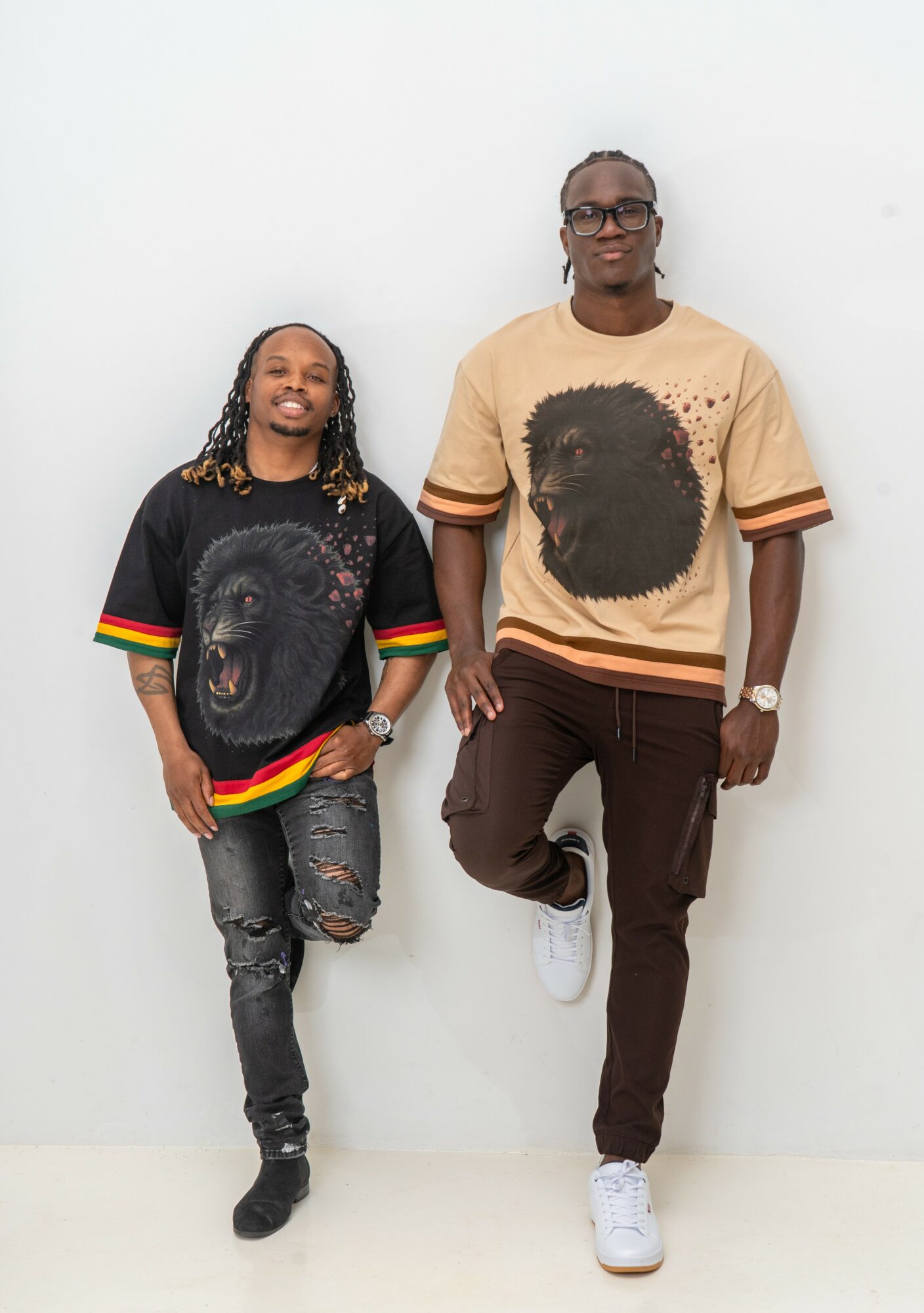 Two people standing against a plain white wall, wearing matching black and beige shirts with animal face designs.