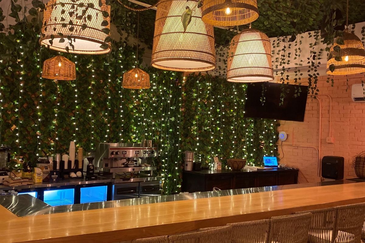 Bar area with hanging lamps, string lights, and a wall of greenery behind the counter.