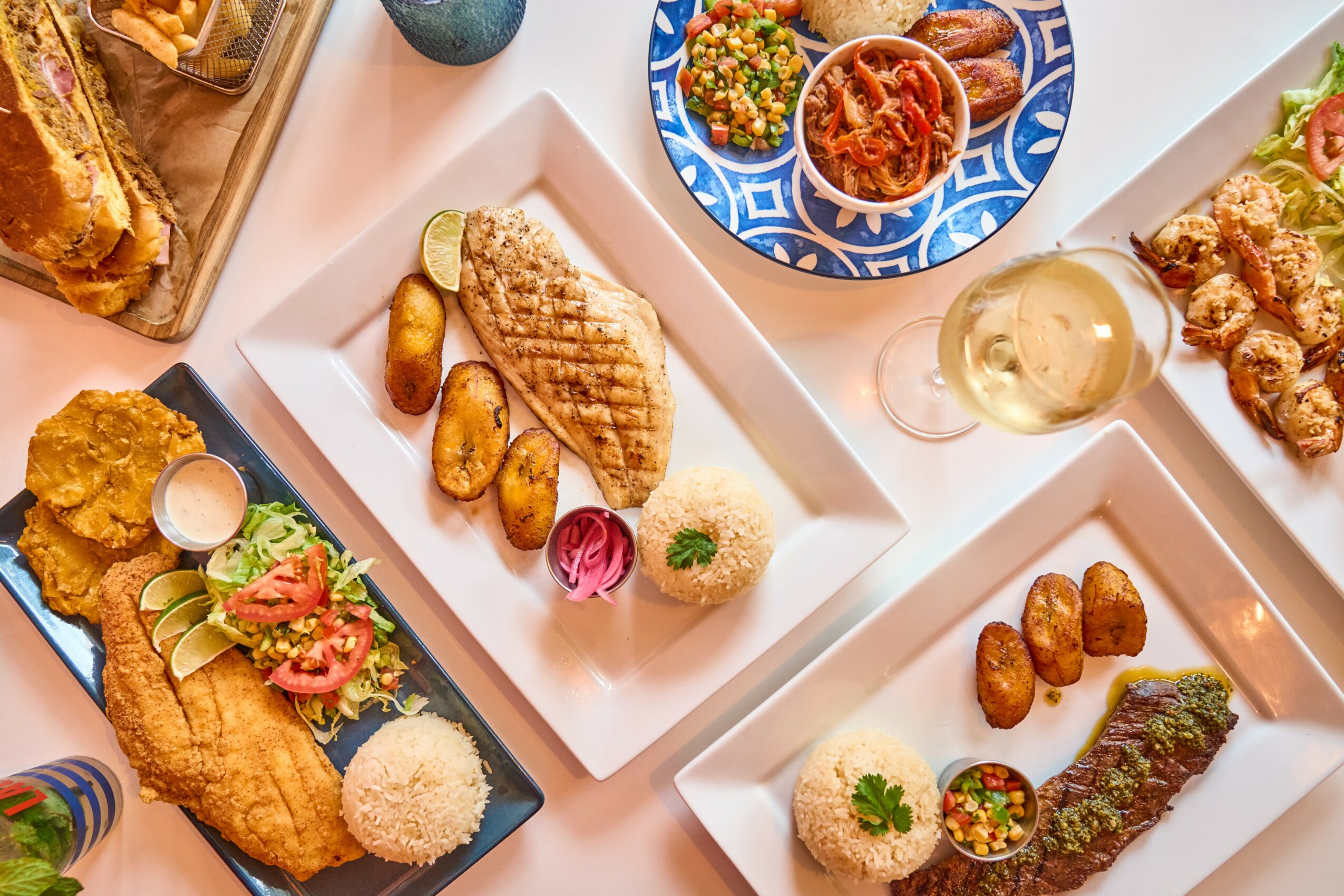 Assorted dishes including fried fish, grilled chicken, roasted potatoes, rice, and vegetables on white and black plates.