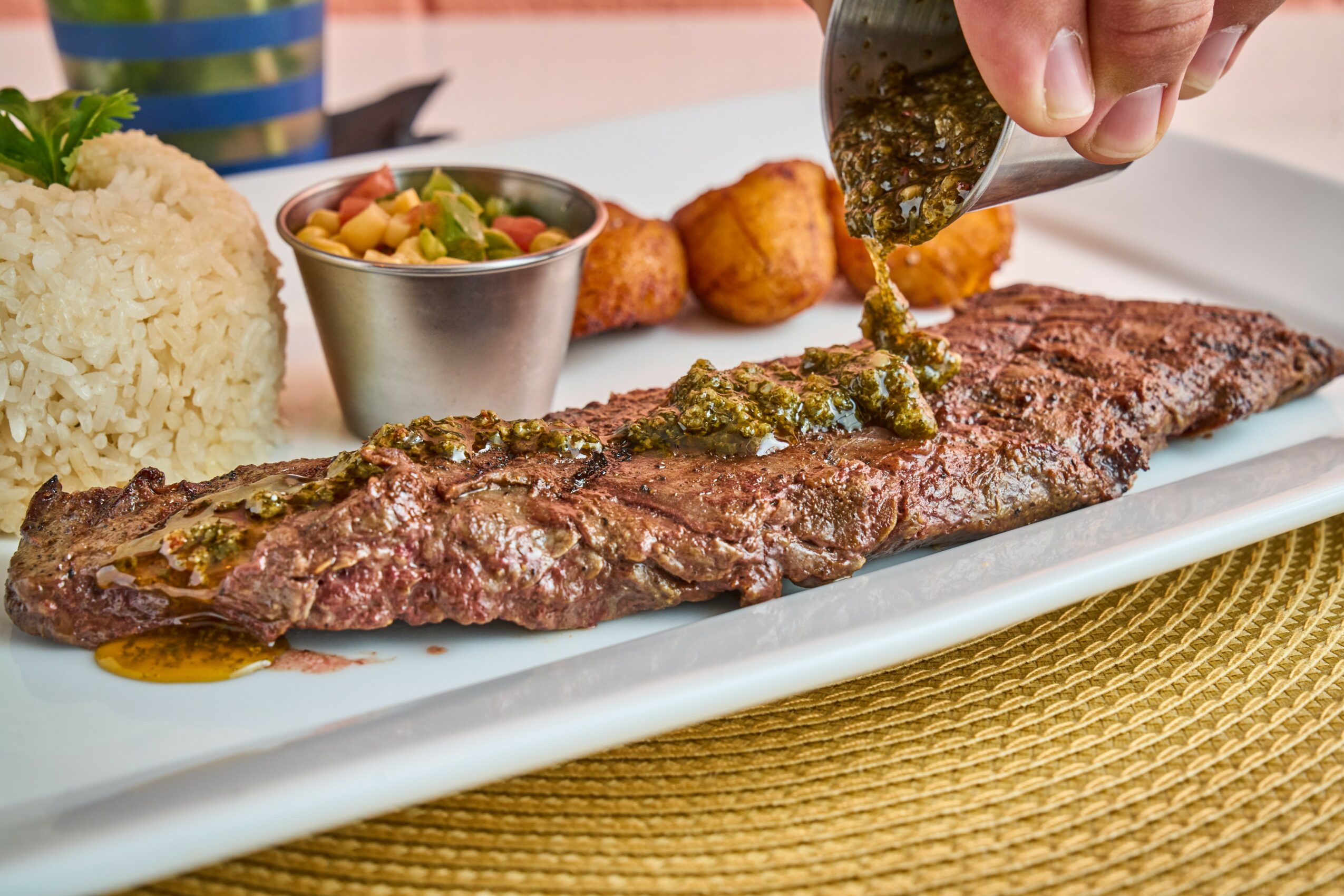 Steak with sauce being poured, rice, vegetables, and fried items on a white plate.