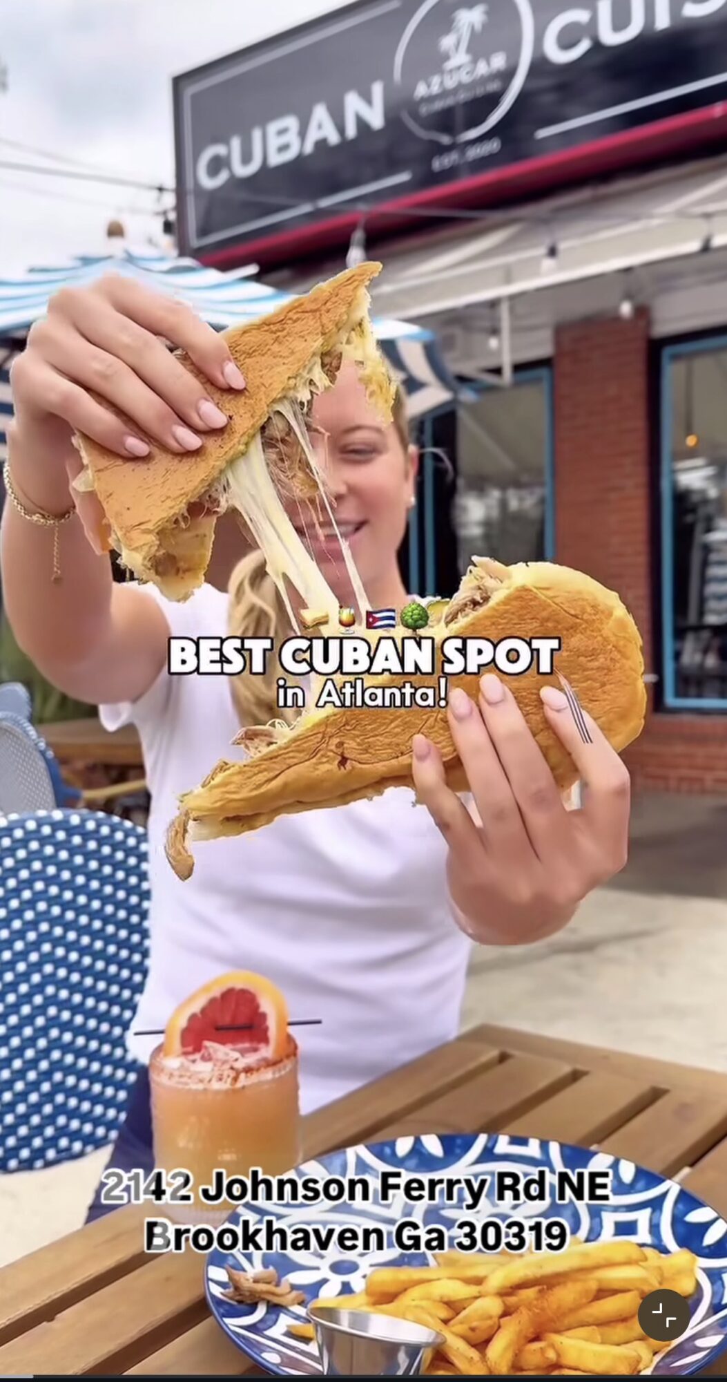 Person holding two sandwiches with cheese and fried chicken outside a restaurant, with a sign reading 'CUBAN' in background.