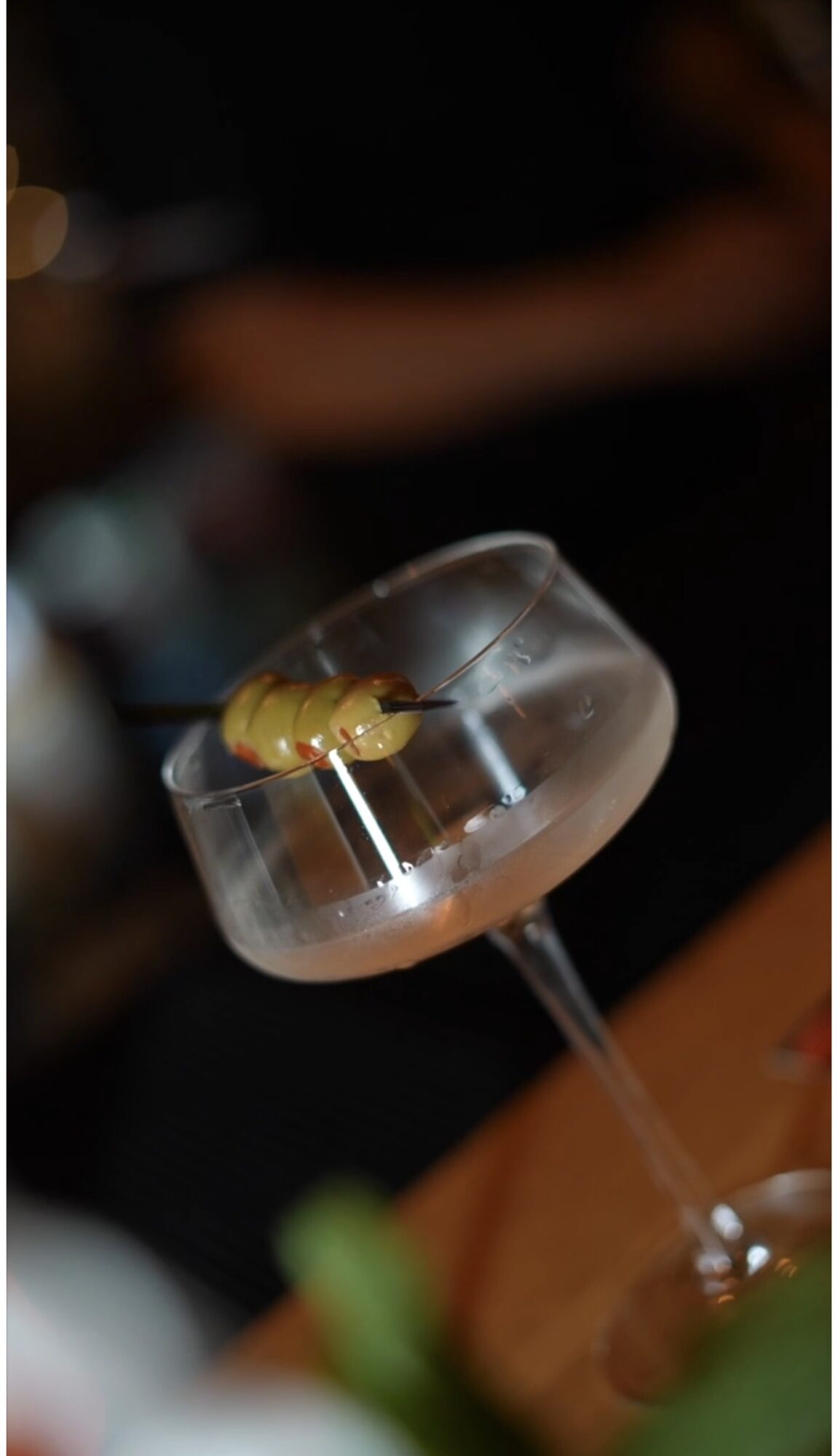 A cocktail glass with a yellow garnish on top, set against a dark background.