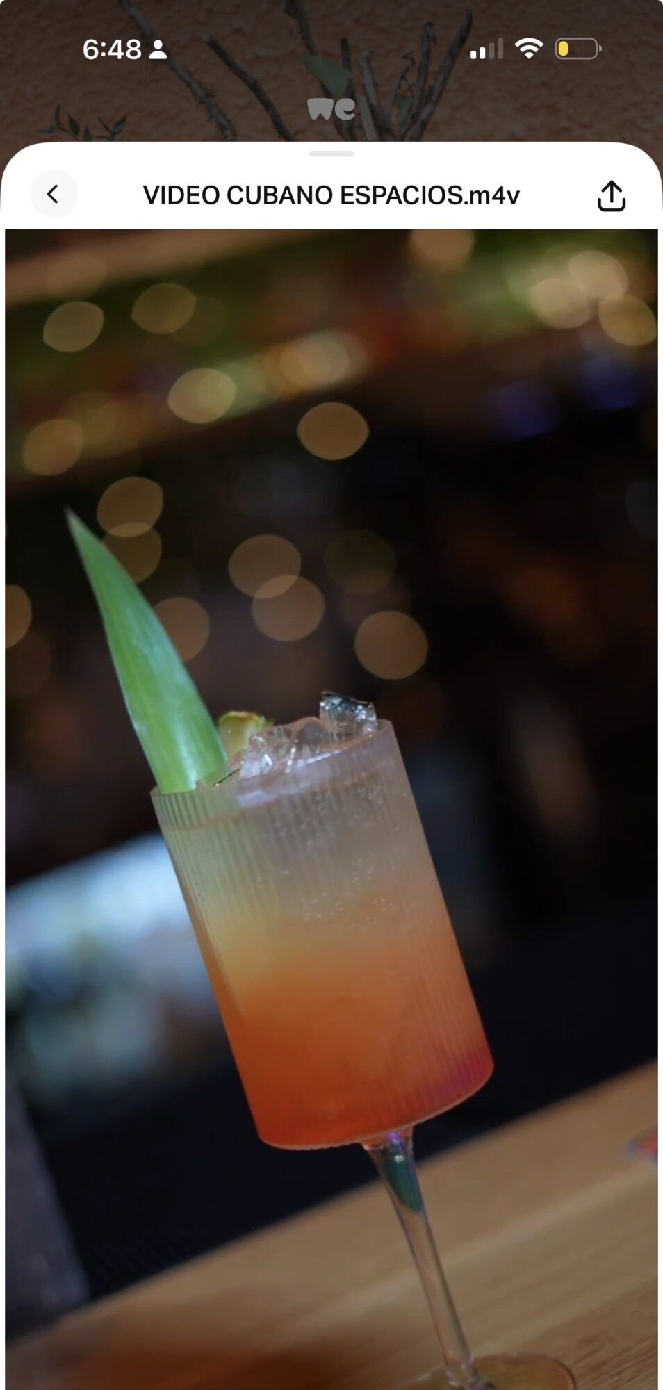 Colorful cocktail in a tall glass with a green straw, blurred background with bokeh lights.
