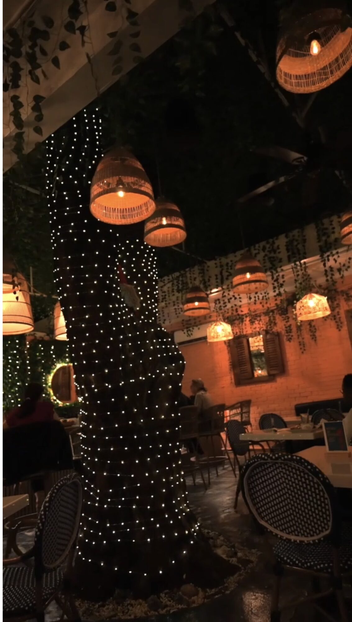 Indoor space with hanging lights, tables, and chairs, illuminated with warm lighting and decorative elements.