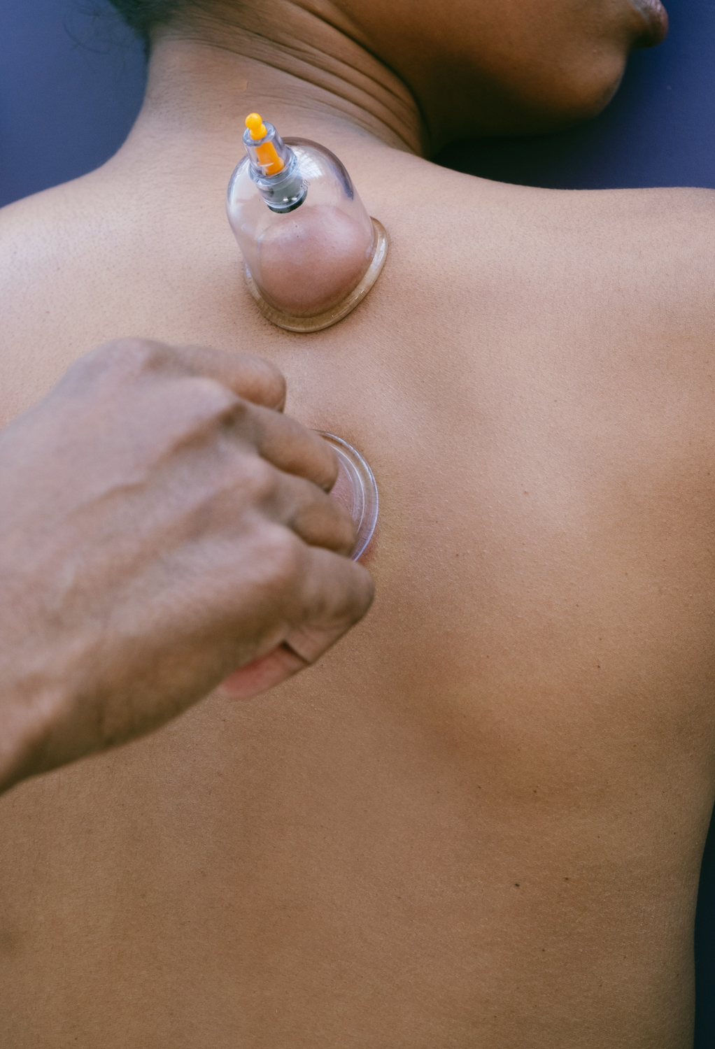 Person receiving medical injection in shoulder with a syringe and bandage, skin visible, background plain.
