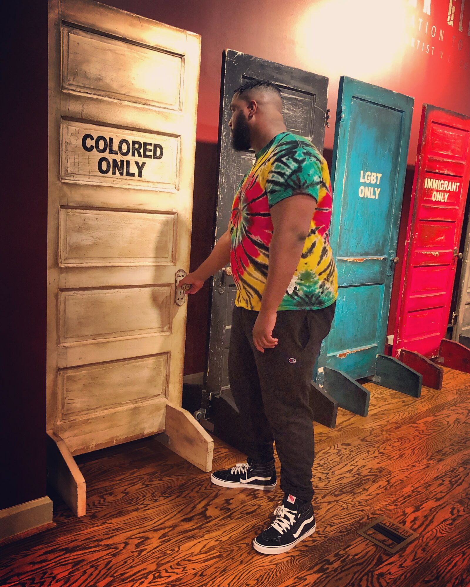 Person opening a door labeled 'Colored Only' in a room with other colored doors.