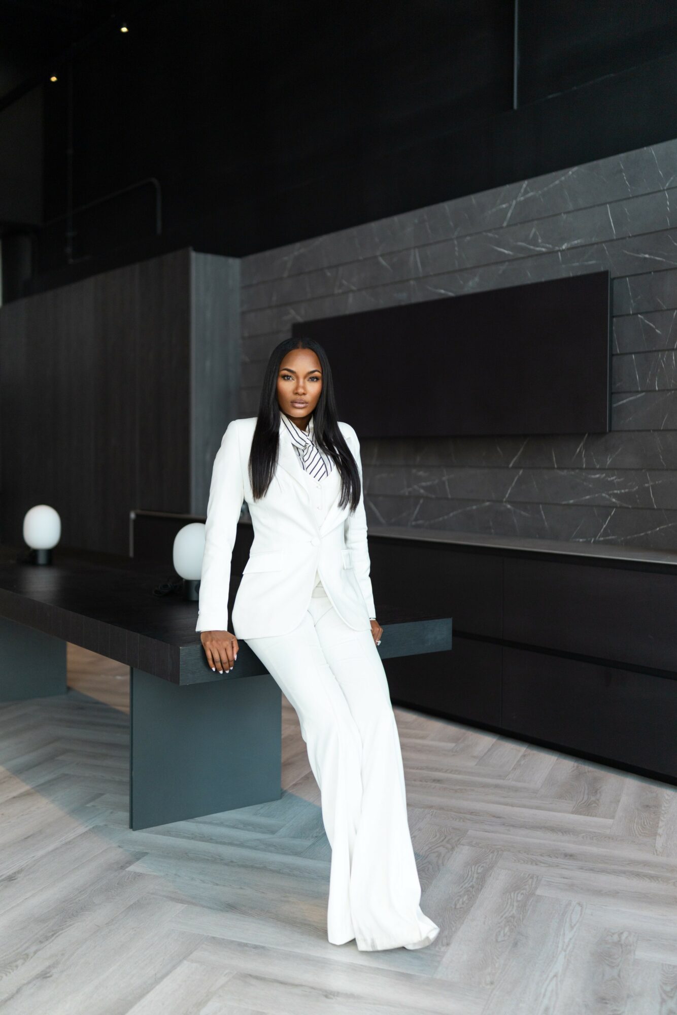 Woman in white suit standing in modern interior with dark walls and light-colored floor.