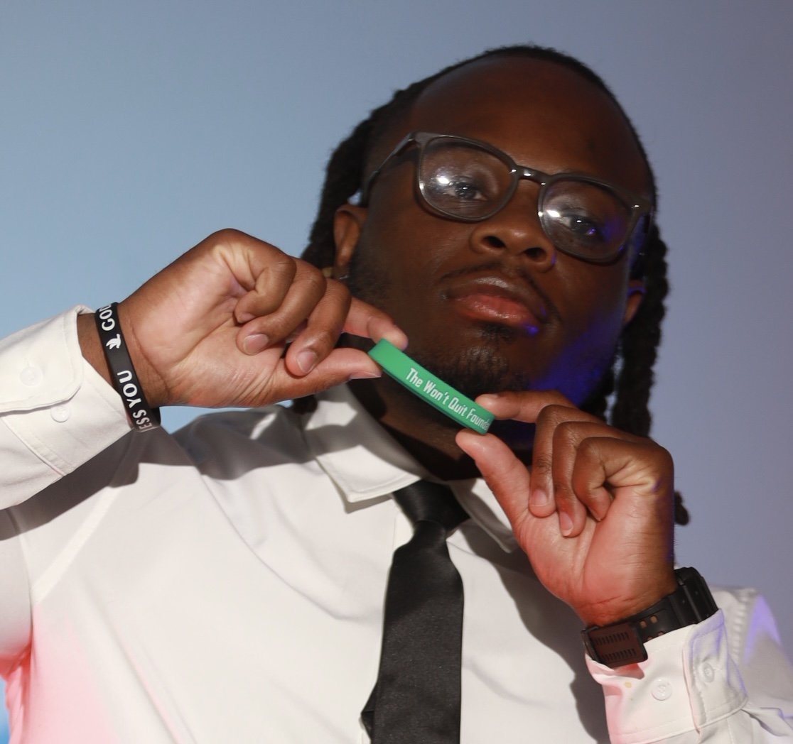 Person with glasses holds a green item near their neck, wearing a white shirt and black tie.