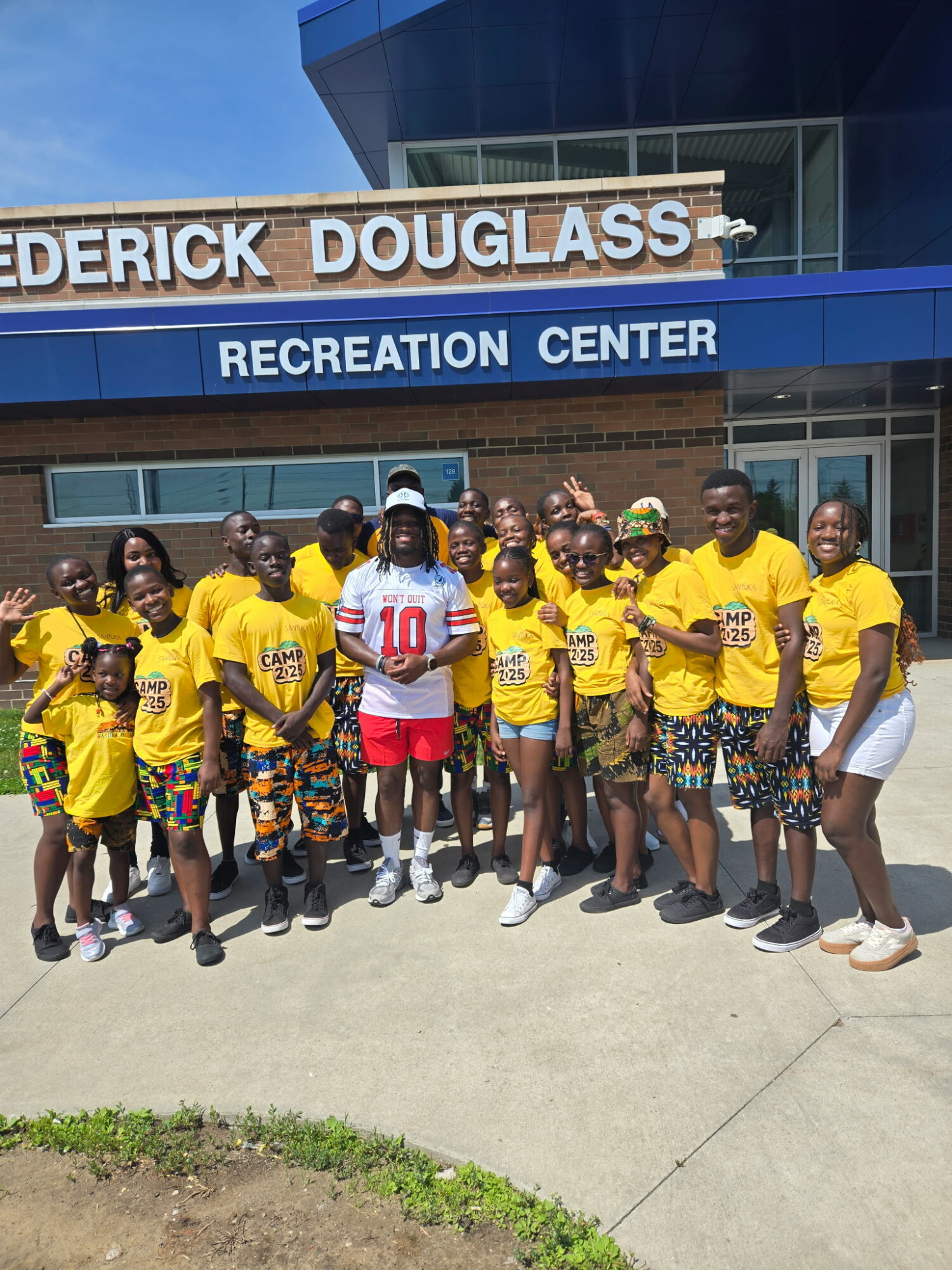 Group of children and adults in yellow shirts standing outside a recreation center building.