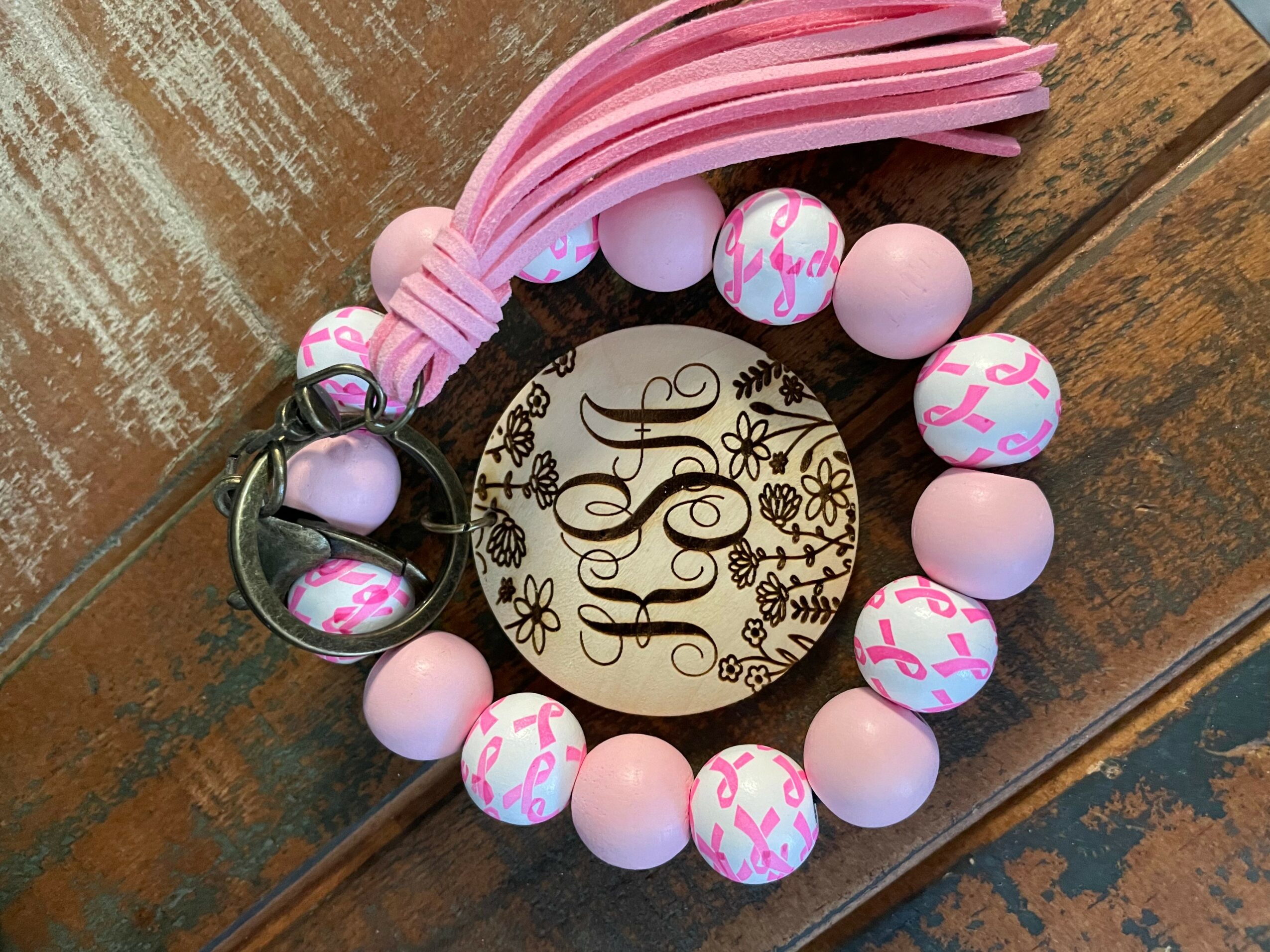 Pink and white beaded bracelet with a round charm on a wooden surface.