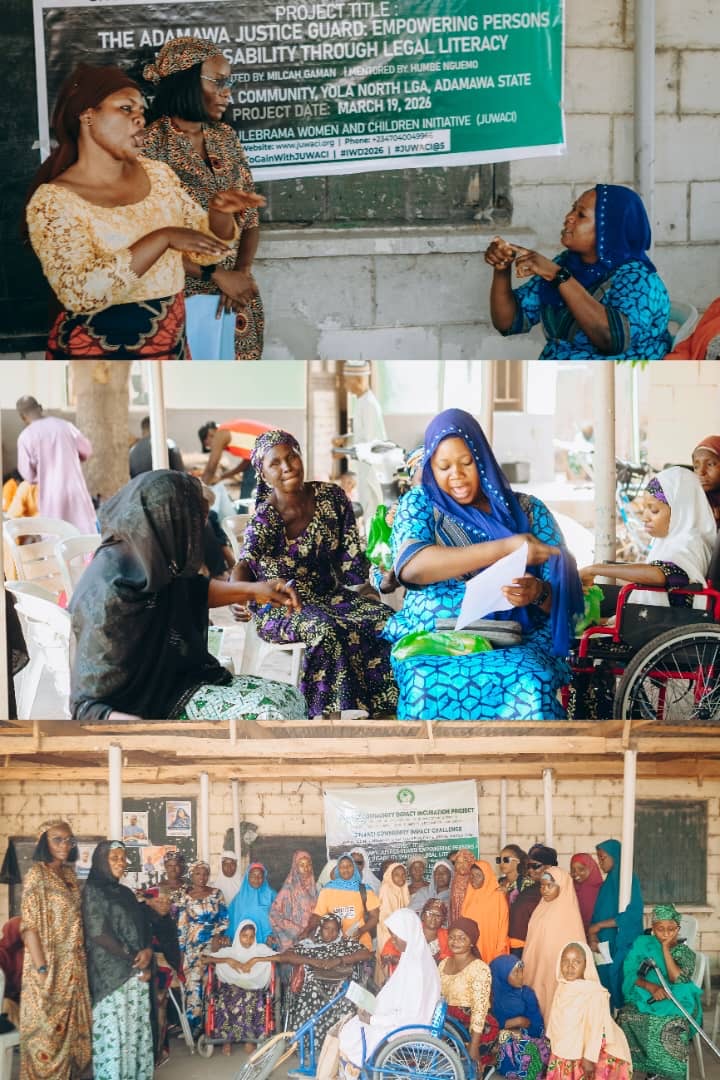 Group of women and children sitting and talking indoors, some in traditional clothing, with a banner in the background.
