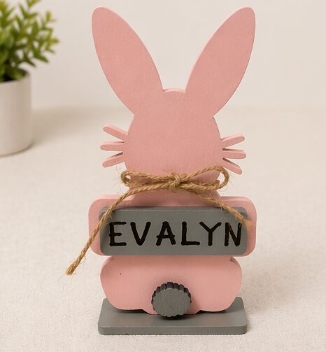 Pink bunny-shaped decoration with a name tag reading 'EVALYN' and a gray base, on a white surface.