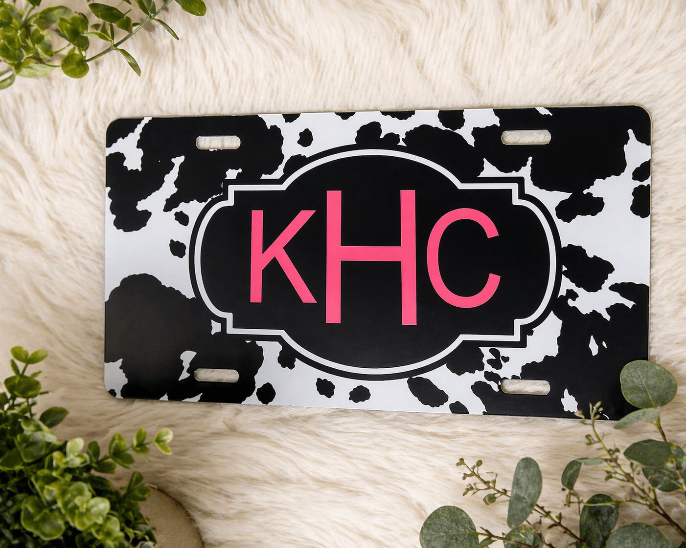Black and white cow print license plate with pink monogram initials 'kHC' in the center.
