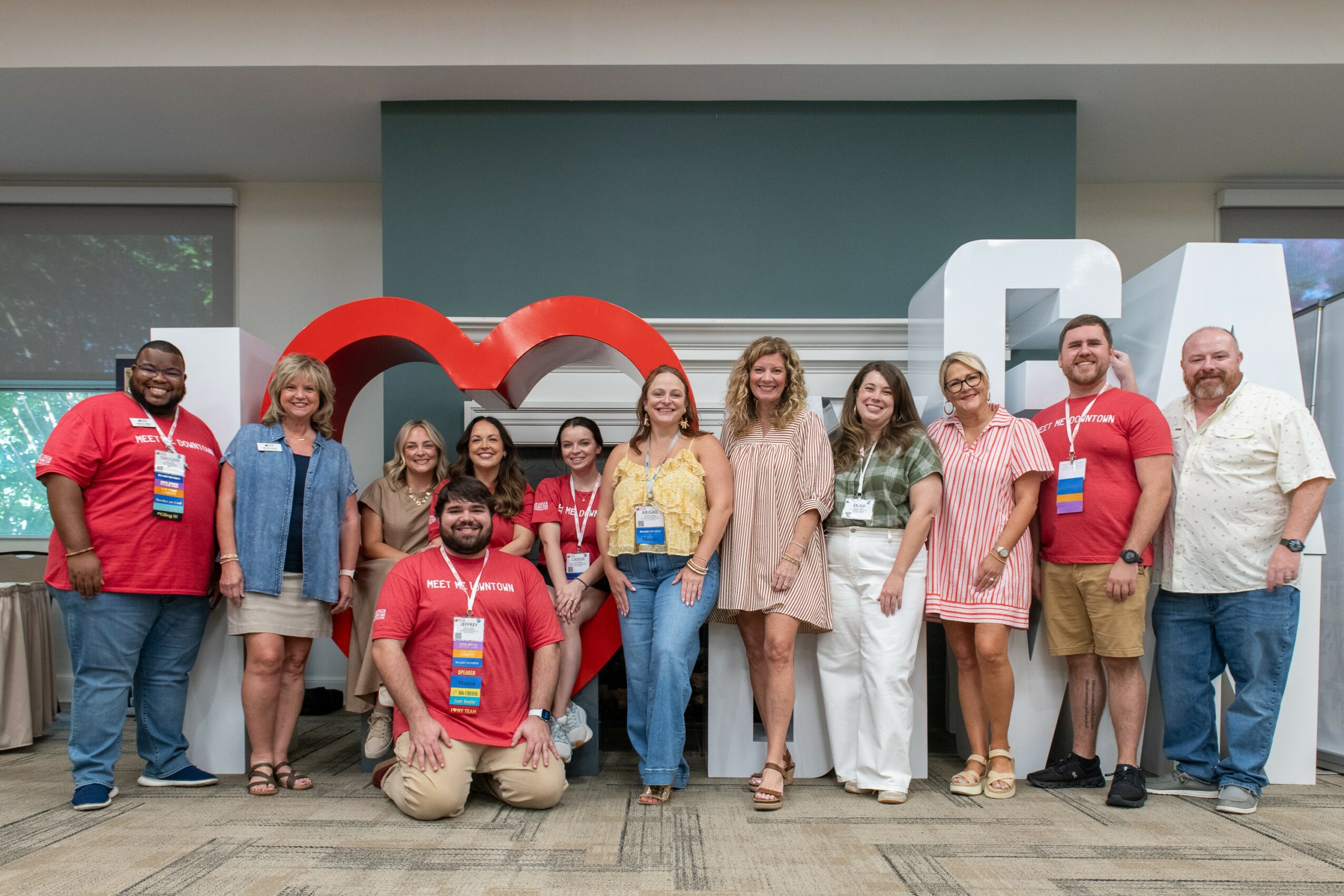 Group of people standing in front of large red and white letters spelling 'LOVE' indoors.
