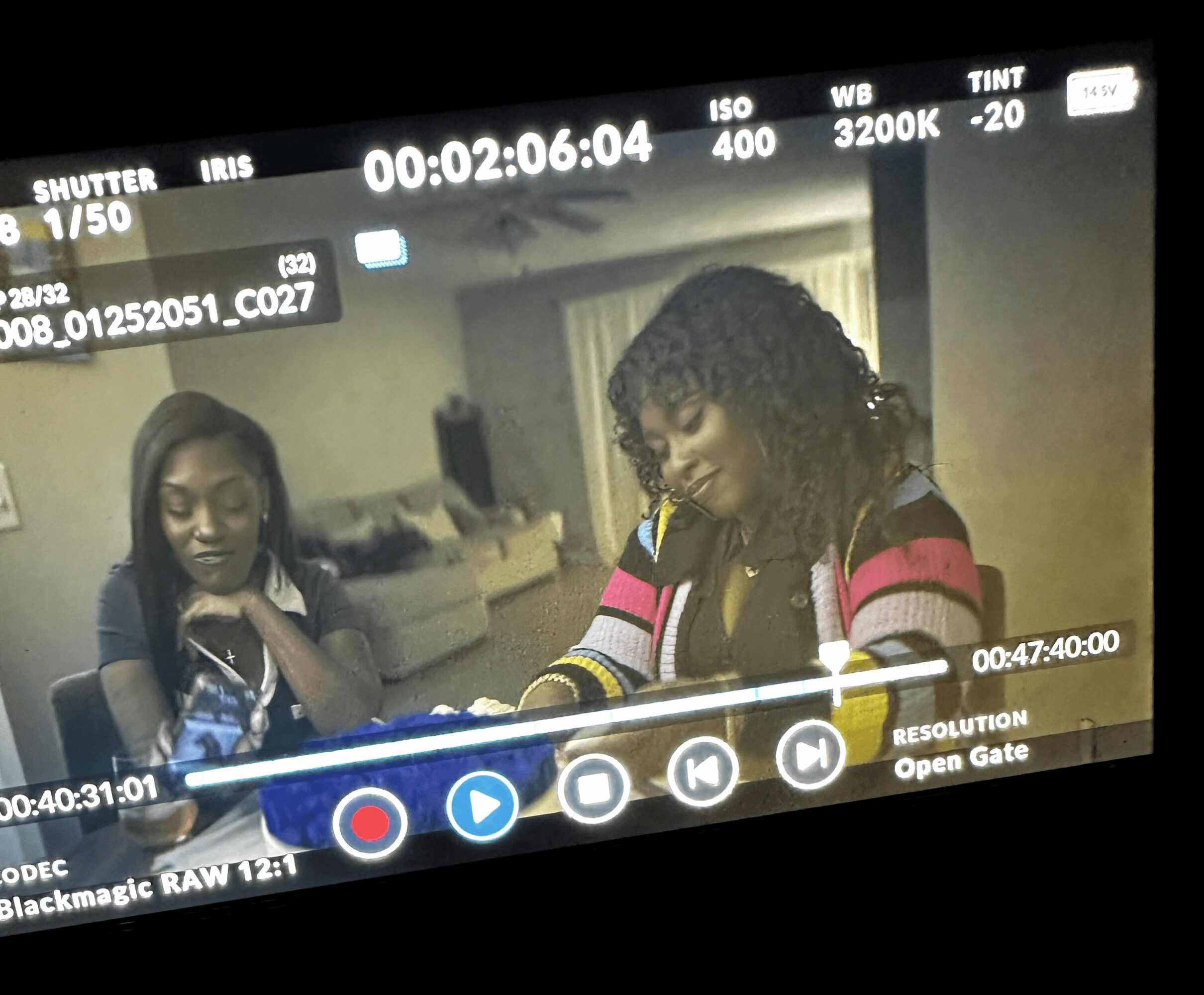 Two women sitting at a table, one with curly hair and colorful striped sweater, the other with straight hair and dark clothing.