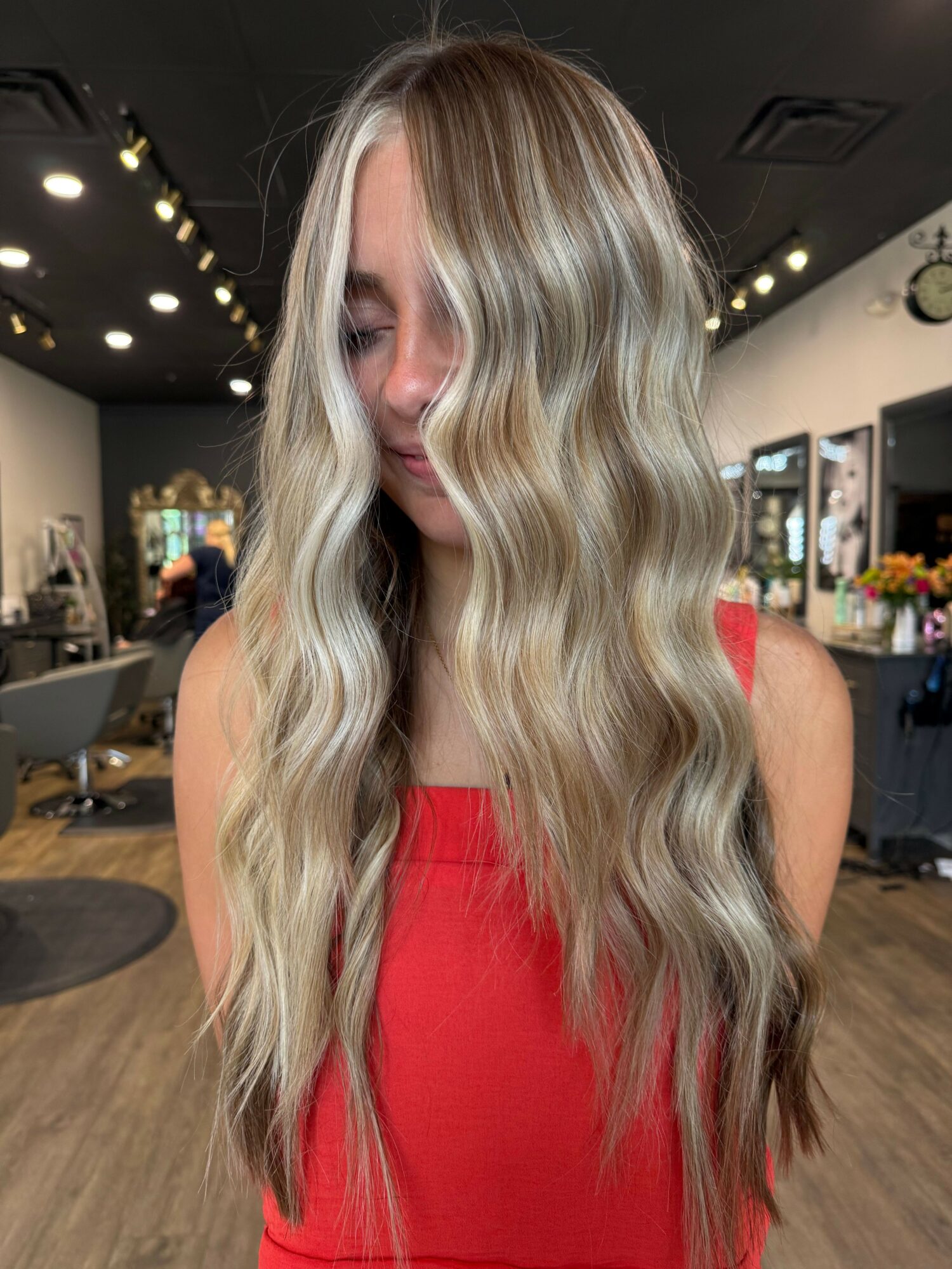 Woman with long, wavy blonde hair wearing a red top in a salon setting.
