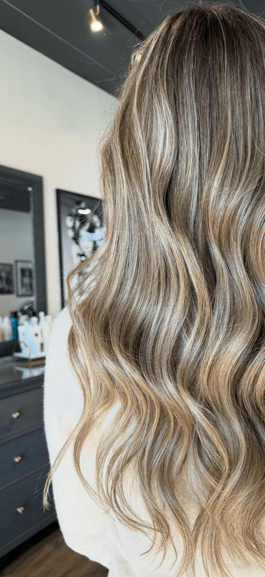 Close-up of a person with long, wavy, blonde hair in a salon setting.