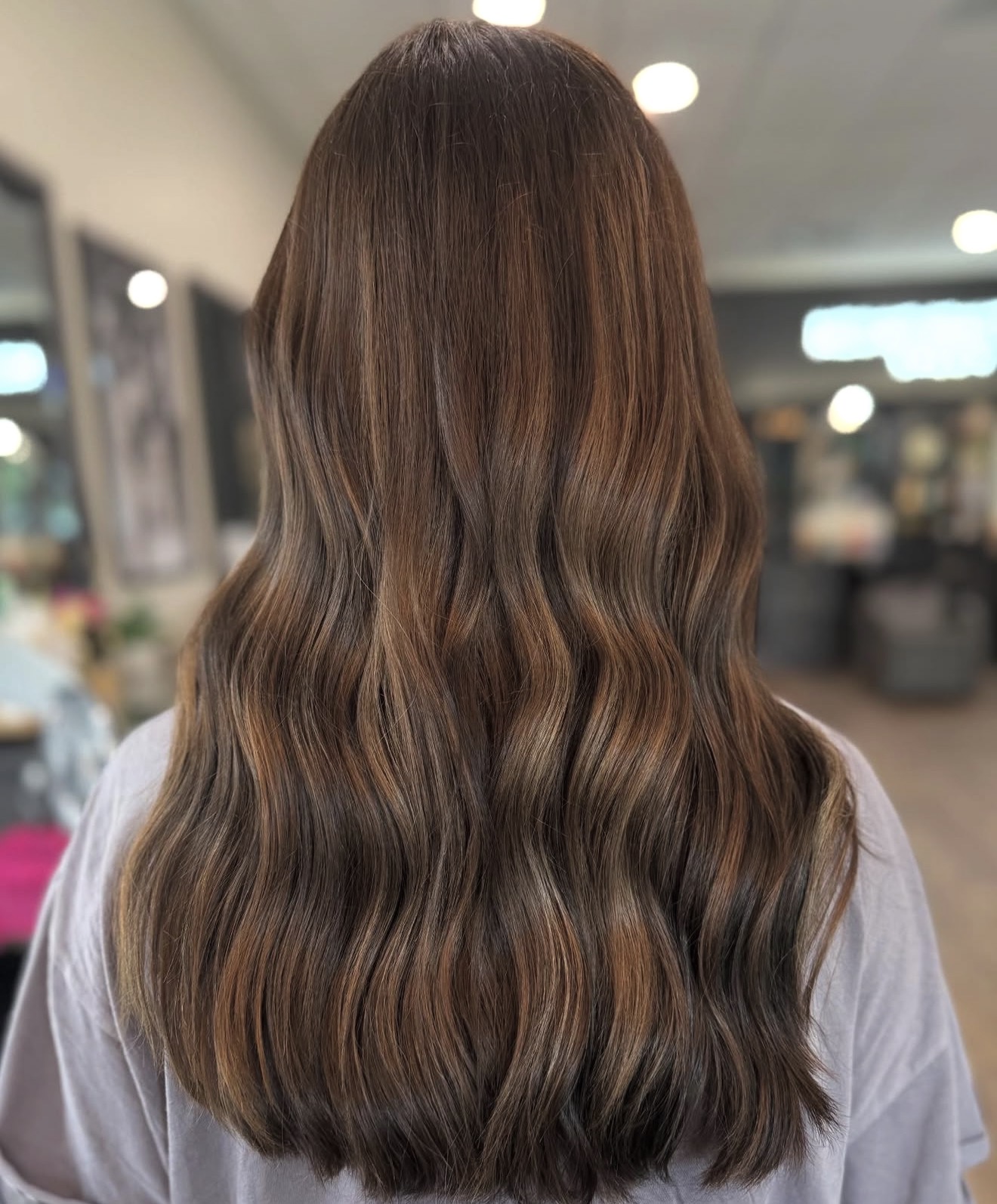 Back of a person with long, wavy brown hair in a salon or indoor setting.