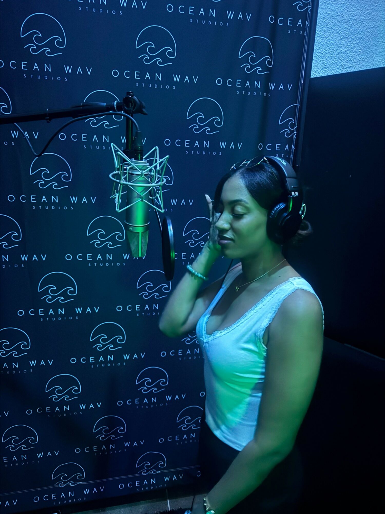 Woman in headphones singing into a microphone in a recording studio with Ocean Wav branding background.