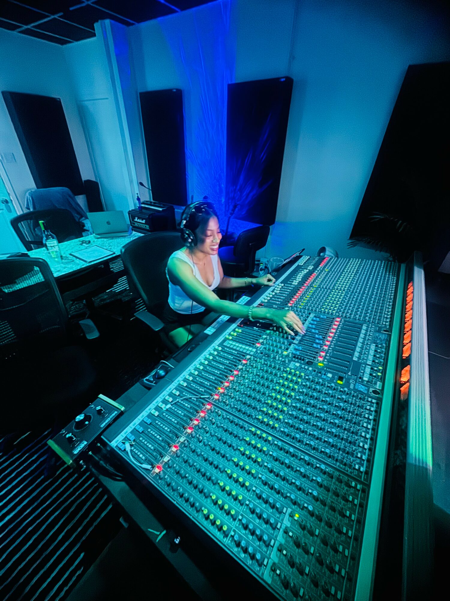 Person working at a large audio mixing console in a recording studio with blue lighting.