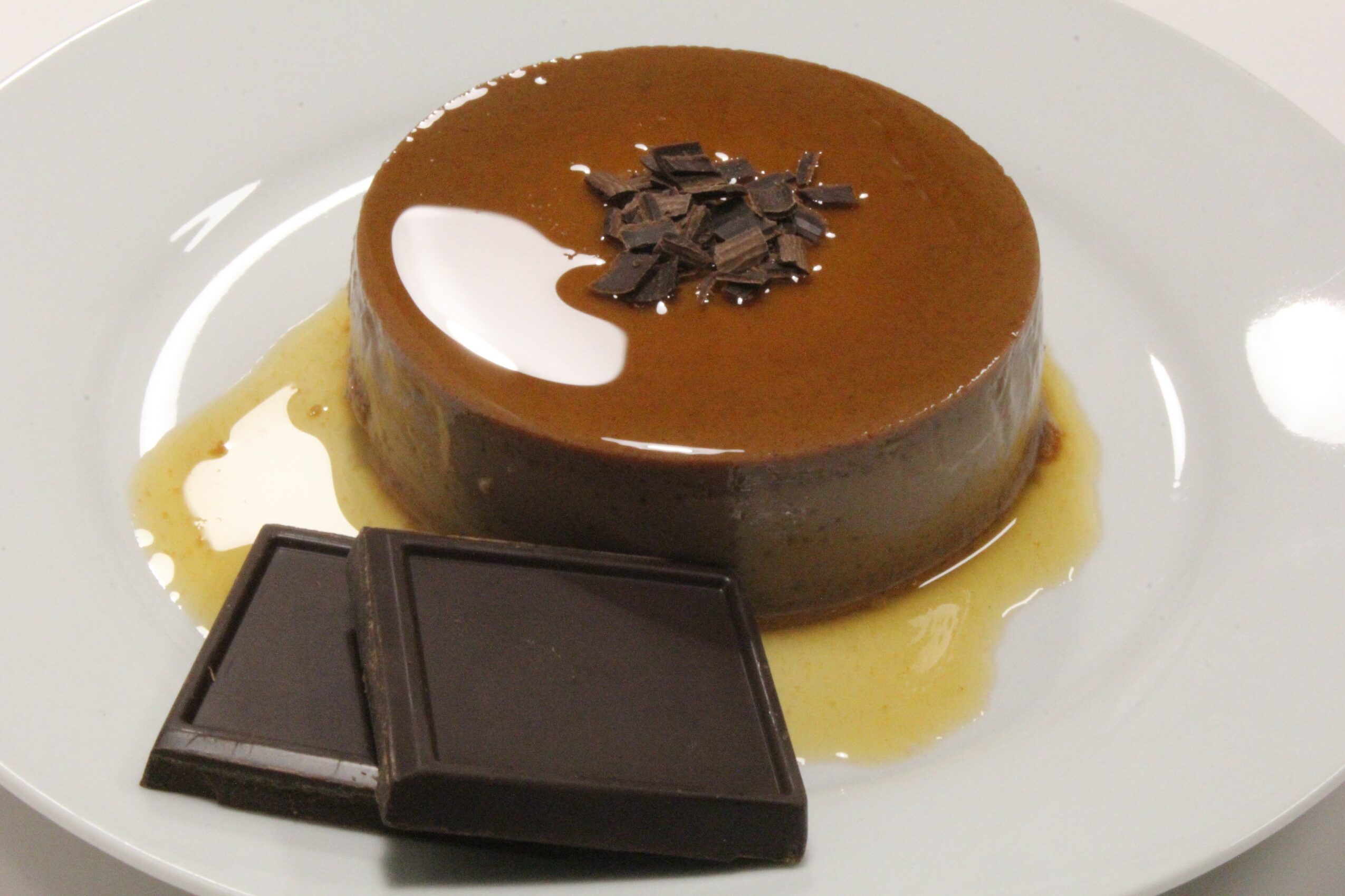 Chocolate dessert with chocolate shavings and sauce on a white plate, two pieces of dark chocolate beside it.
