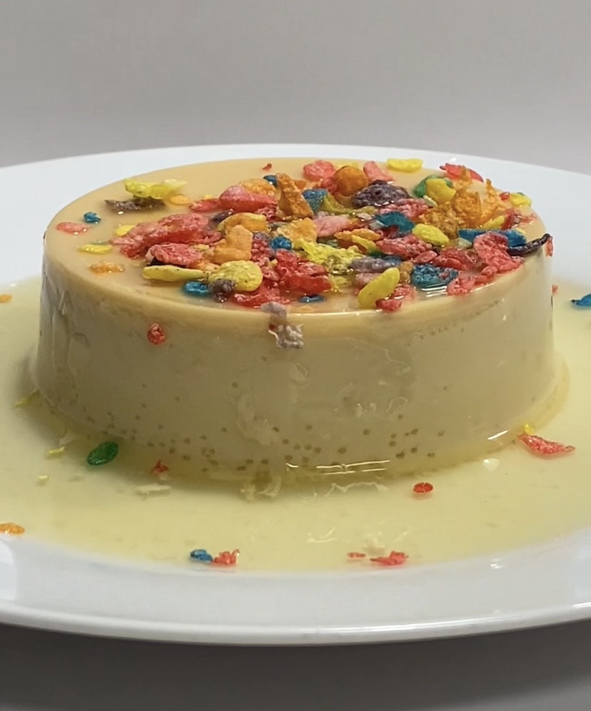 Round cake with colorful sprinkles on top, placed on a white plate with some sprinkles around.