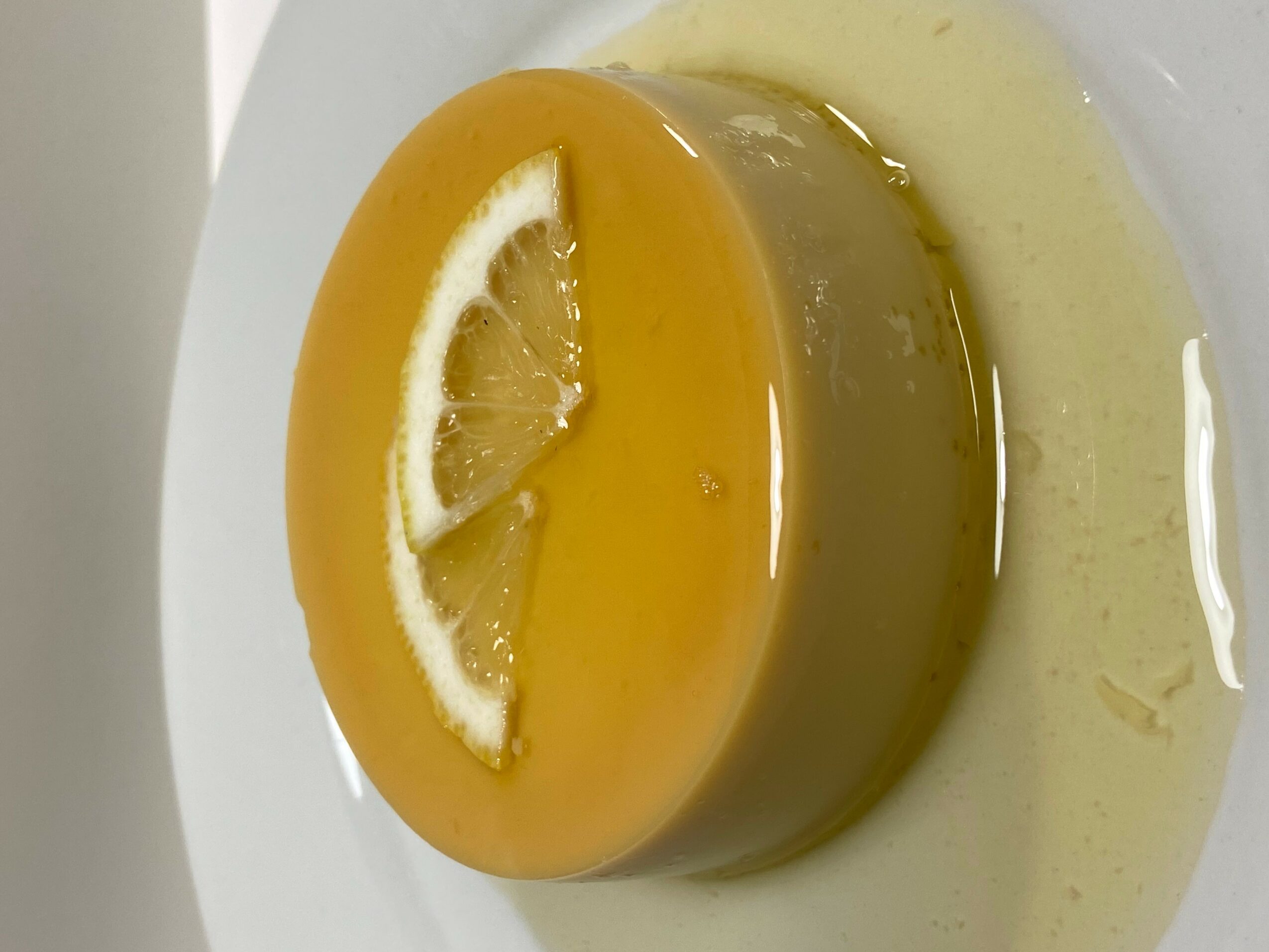 Round yellow dessert with lemon slices on top, on a white plate with sauce around it.