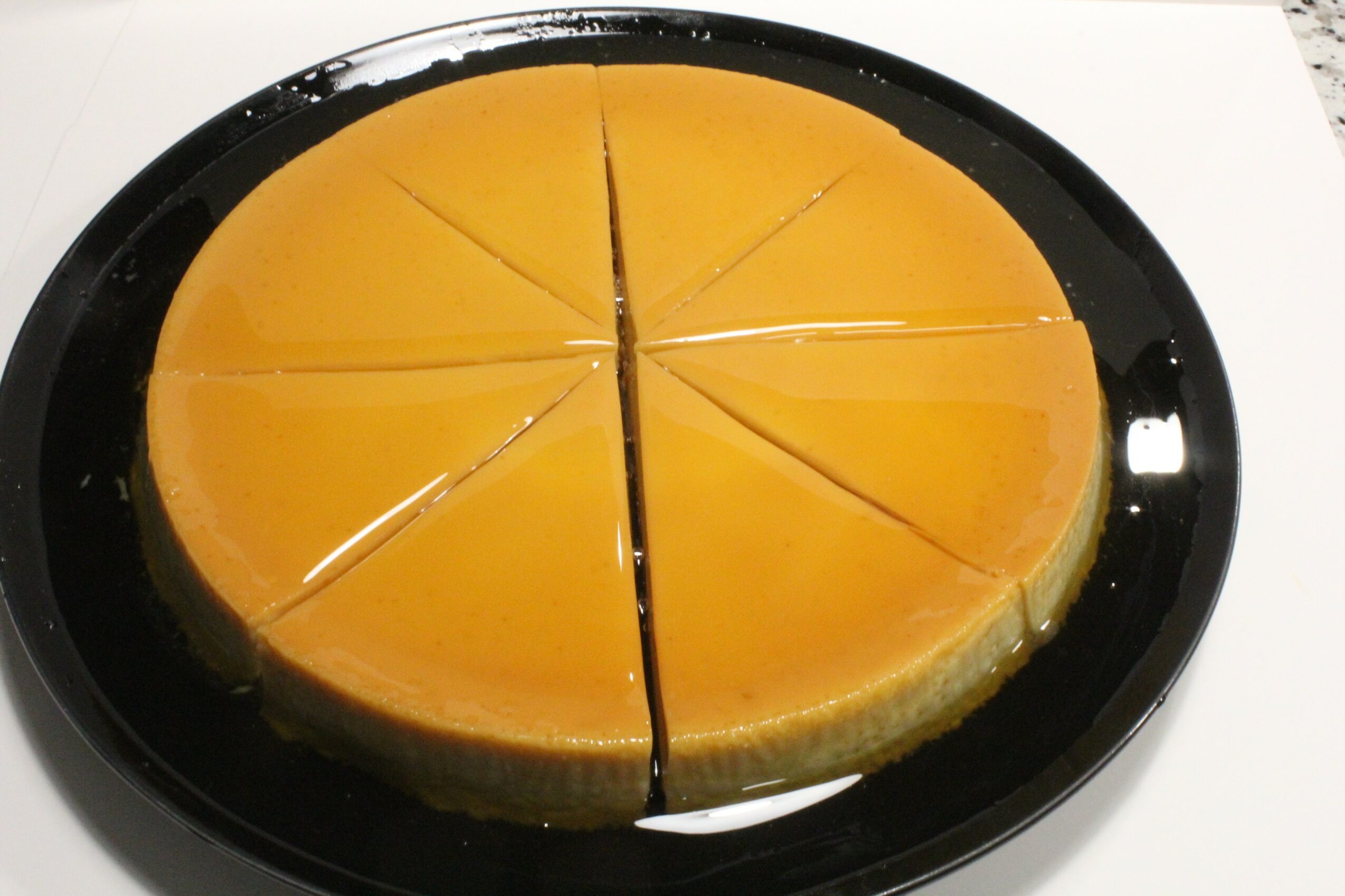 A round cheesecake with eight slices on a black plate, with a yellow-orange topping and a crust at the edge.