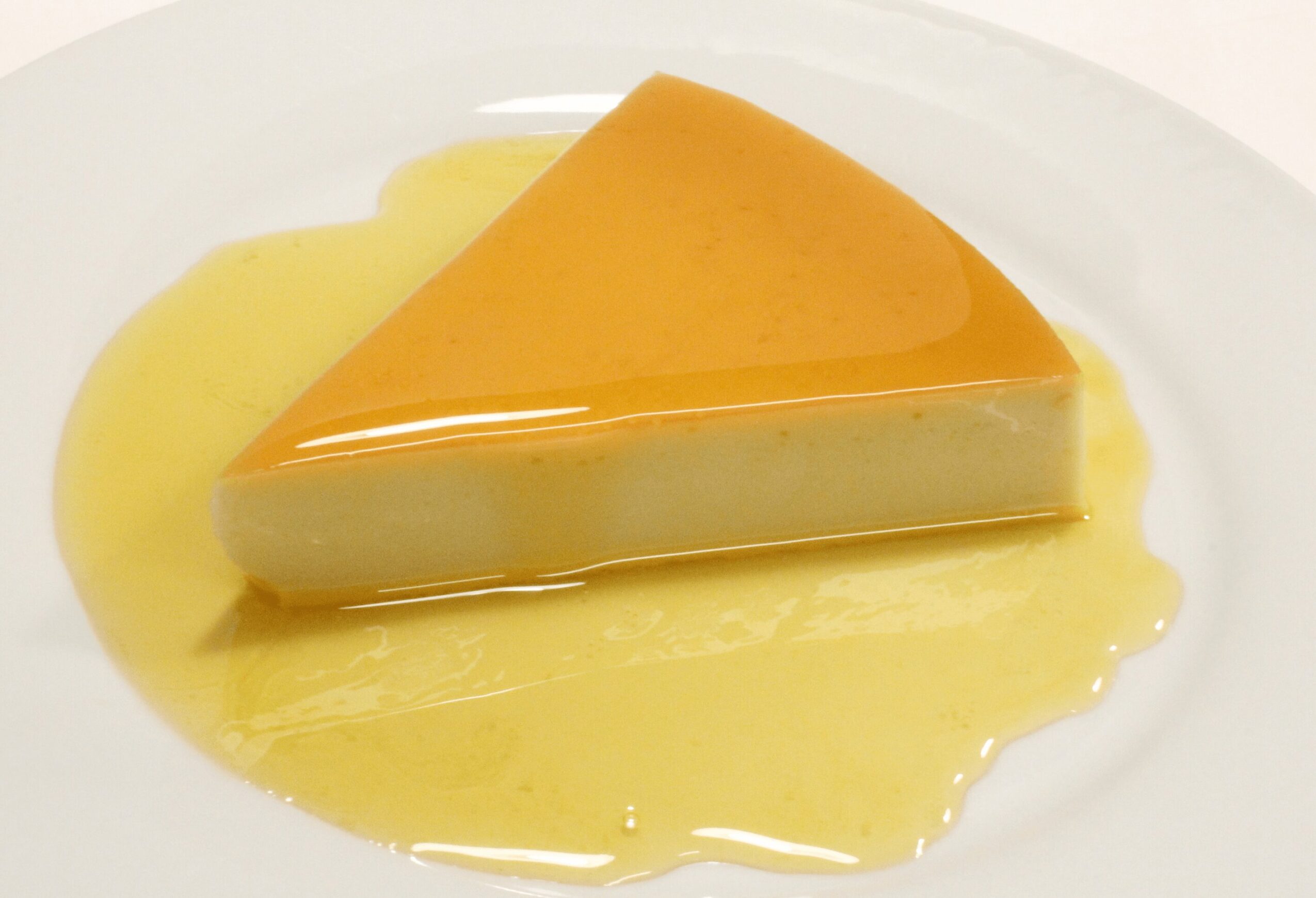 Slice of caramel flan with caramel sauce on white plate.