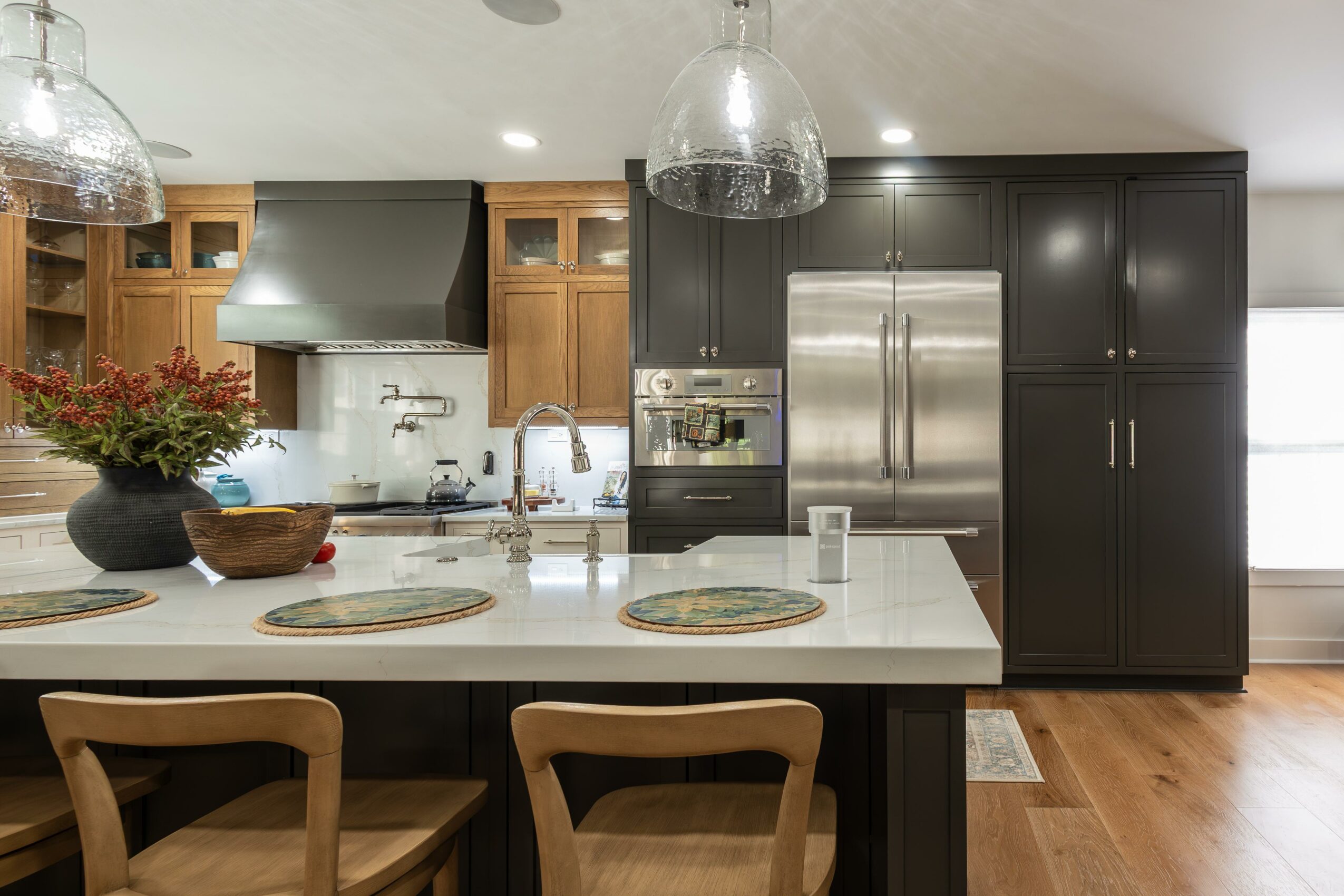 Kitchen with white island, wooden and black cabinets, stainless steel refrigerator, and pendant lights.