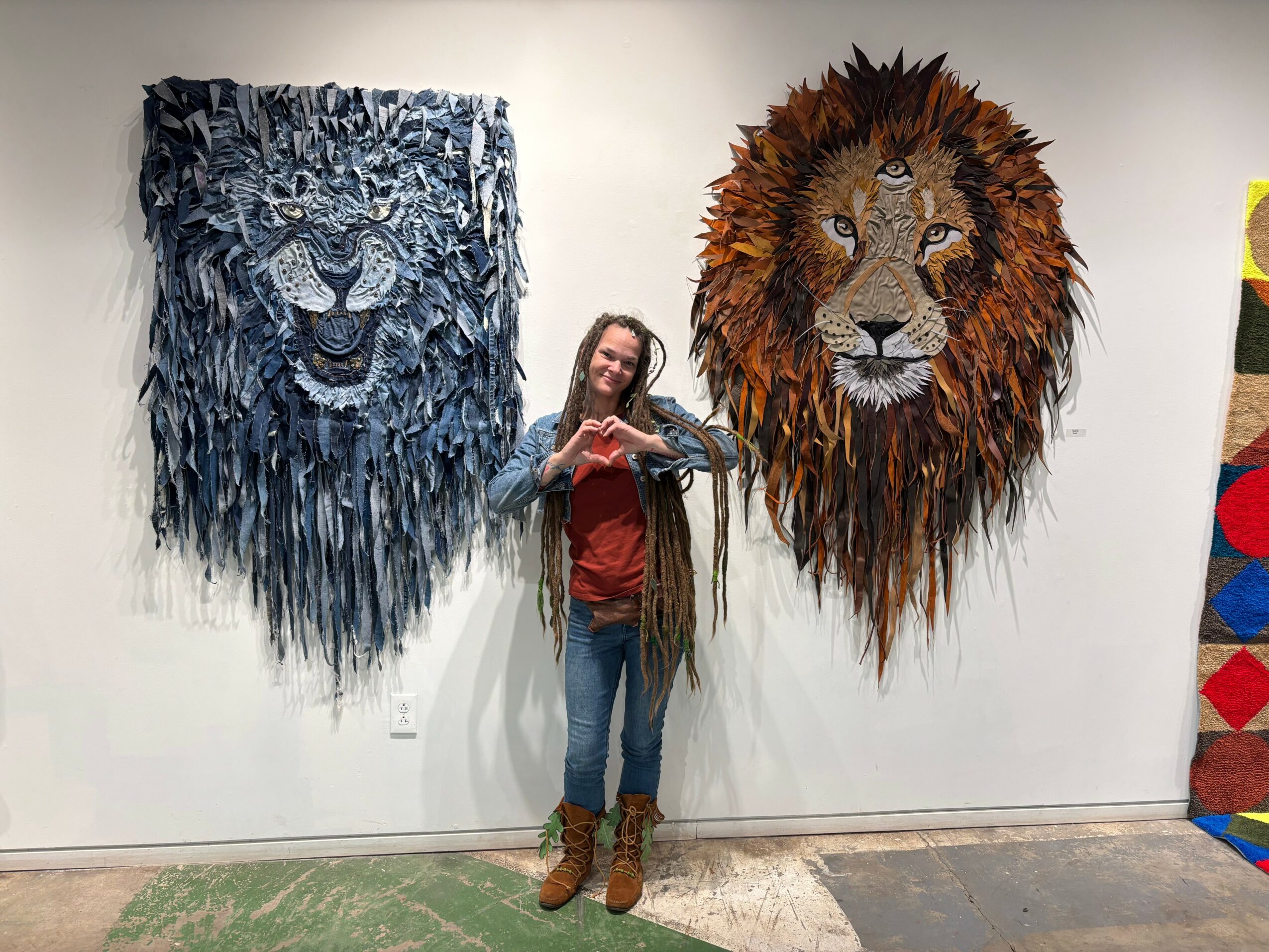 Girl standing between two large lion head wall art pieces, one blue and one brown, making a heart shape with her hands.