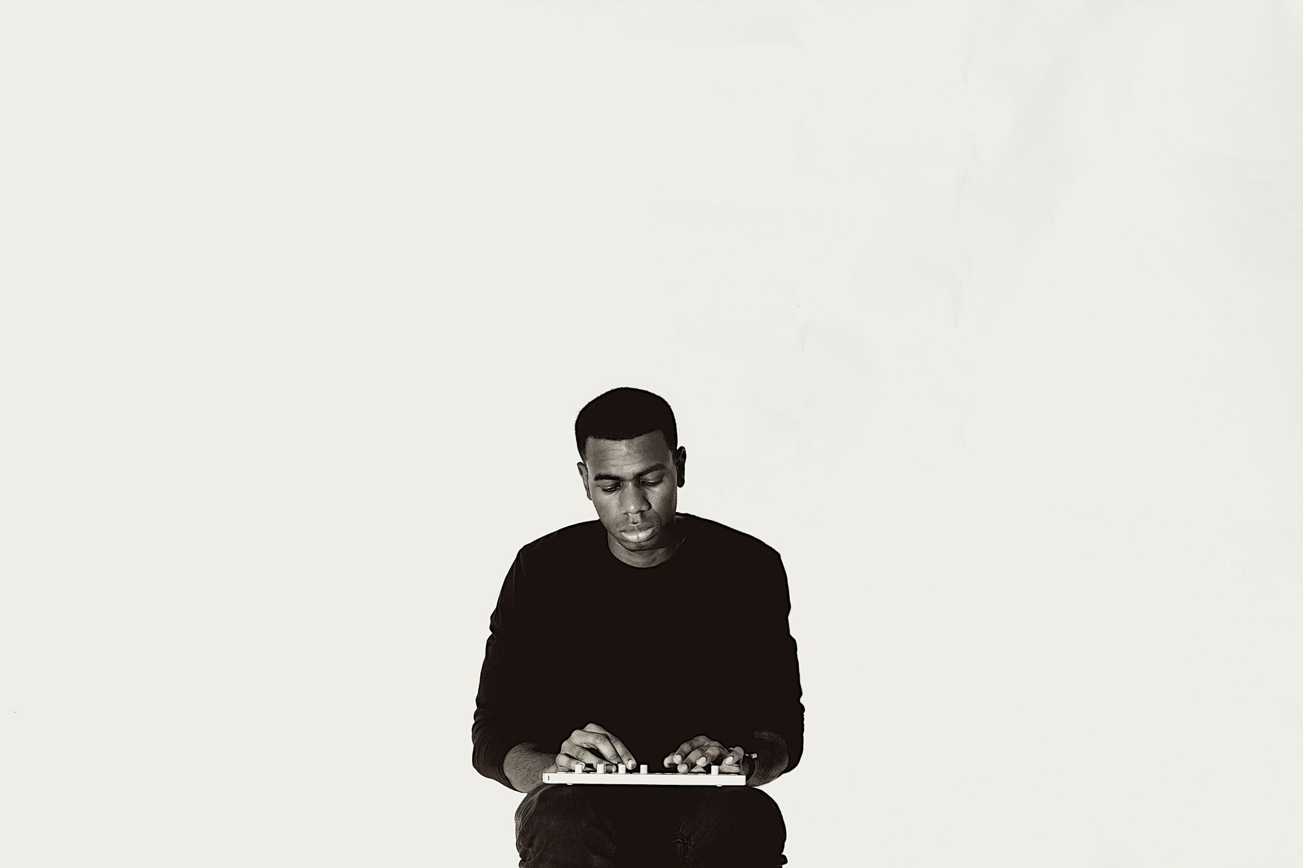 Young man with short hair wearing a dark shirt, looking down, against a plain light background.