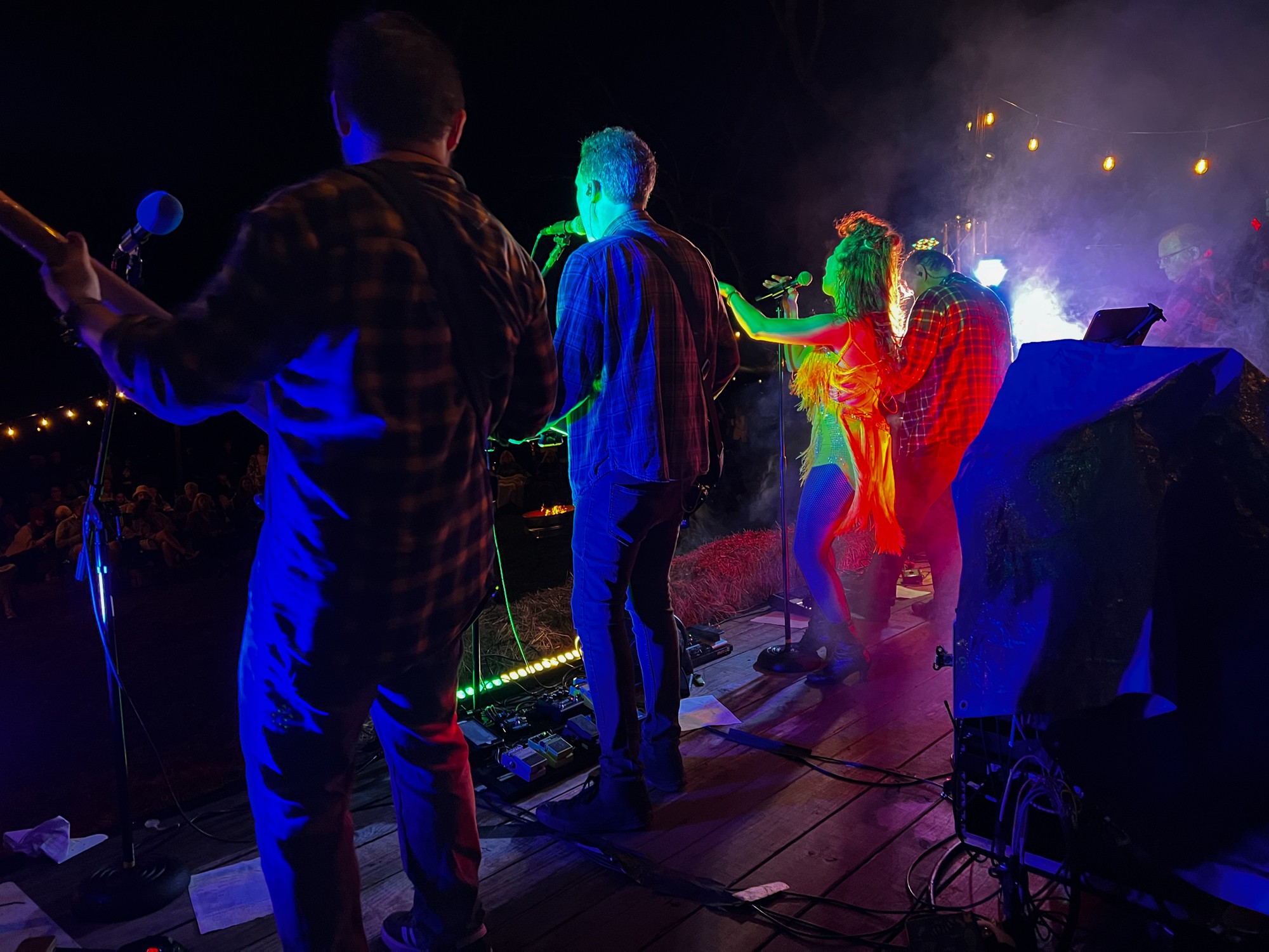 Group of people performing on stage with colorful lighting and smoke effects at night.