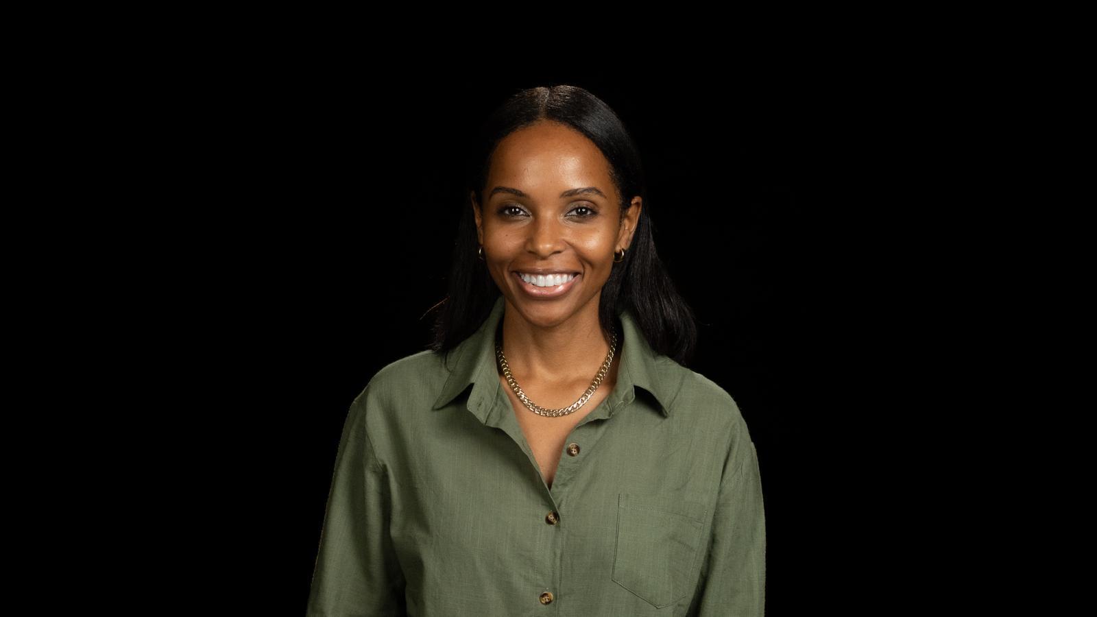 Woman with long dark hair smiling, wearing a green shirt against a black background.