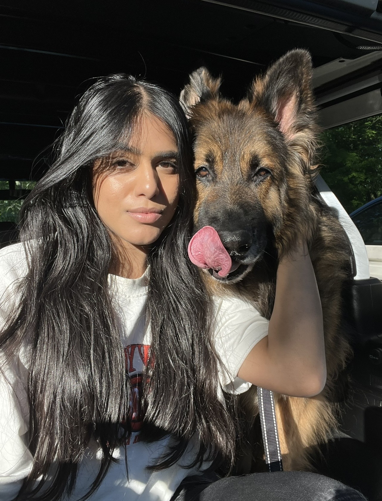 Young woman with long dark hair and a German Shepherd dog inside a vehicle.