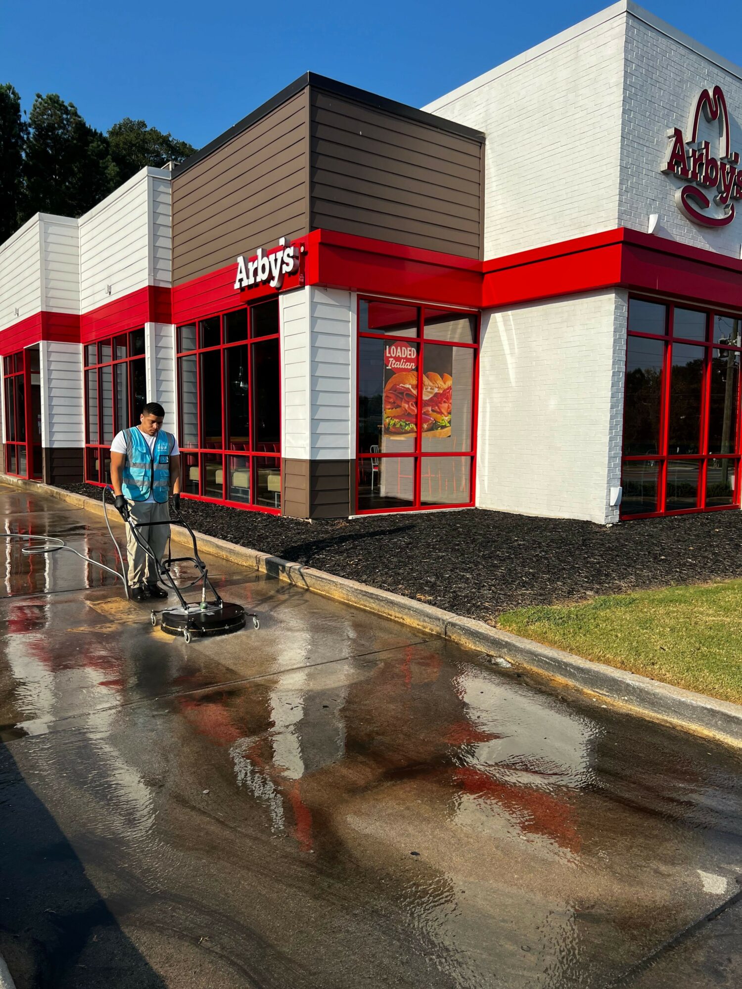 Person cleaning wet pavement outside Arby's restaurant with red and white exterior and large windows.
